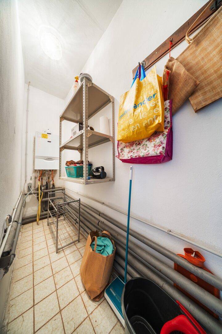 Schmaler Hauswirtschaftsraum mit Gastherme, Regalen und Fliesenboden.