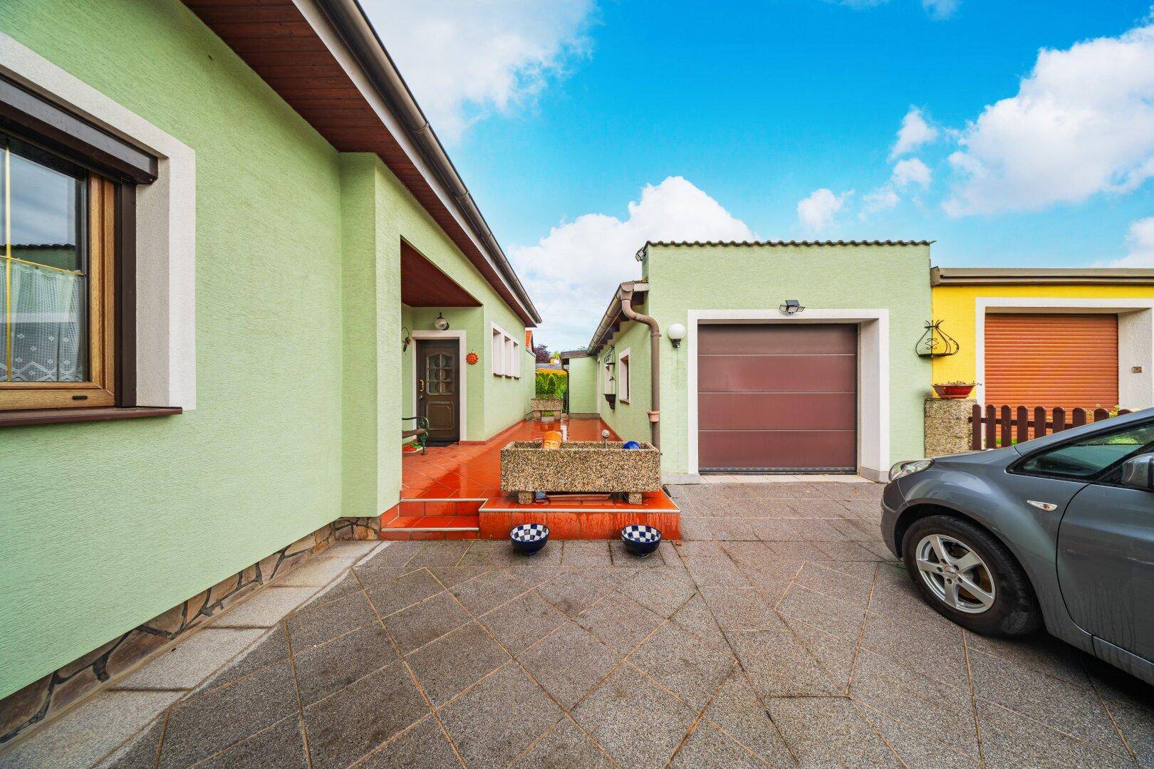 Seitenansicht des Hauses mit Garage, Eingangsbereich und gepflasterter Fläche.