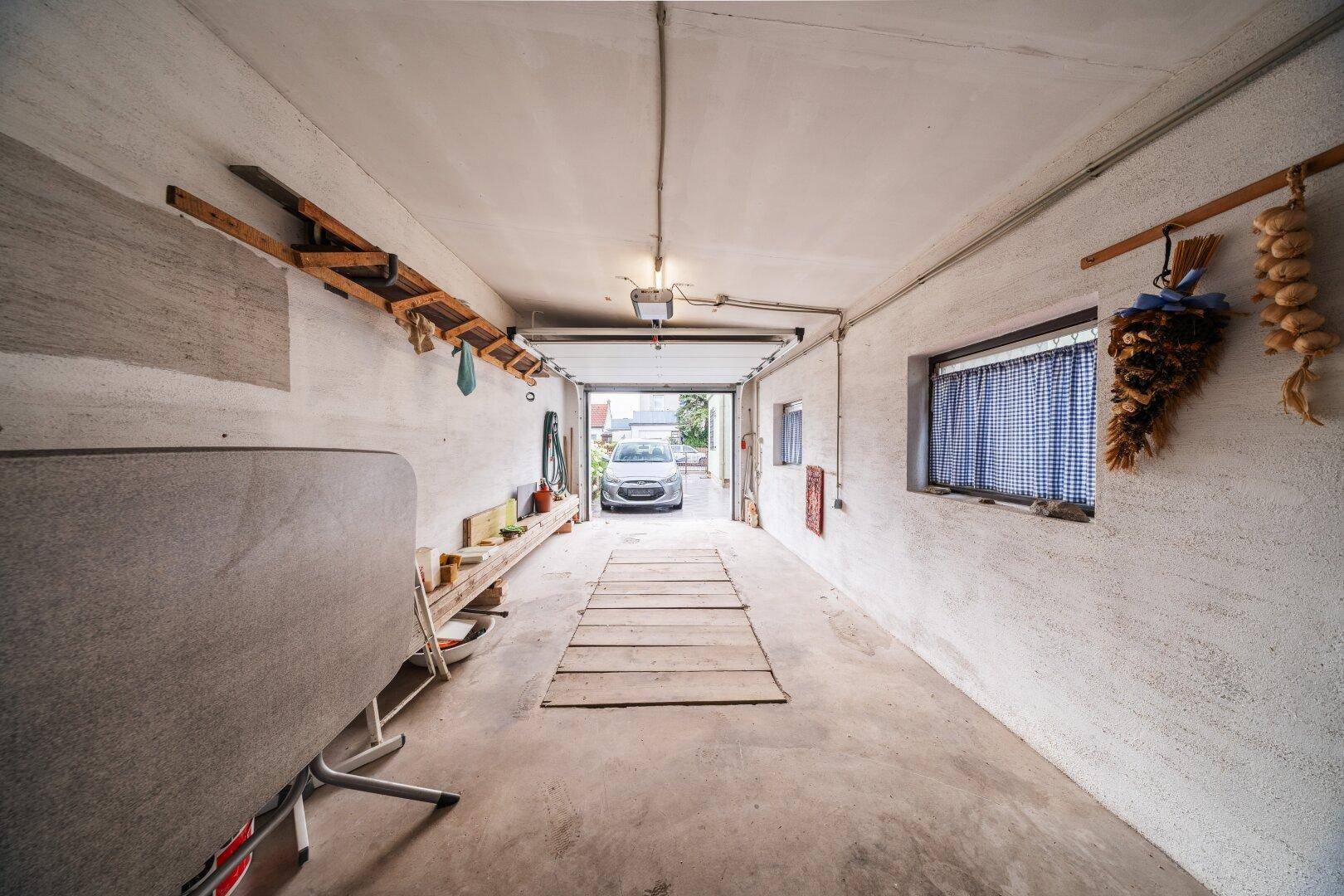 Lange Garage mit Betonboden, Werkbank und Blick auf die Einfahrt.
