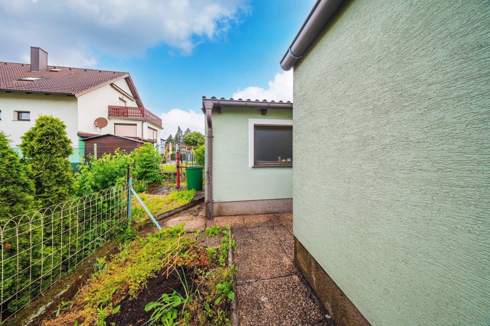 Kleiner Gartenbereich neben dem Haus mit Hecke und Zaun.
