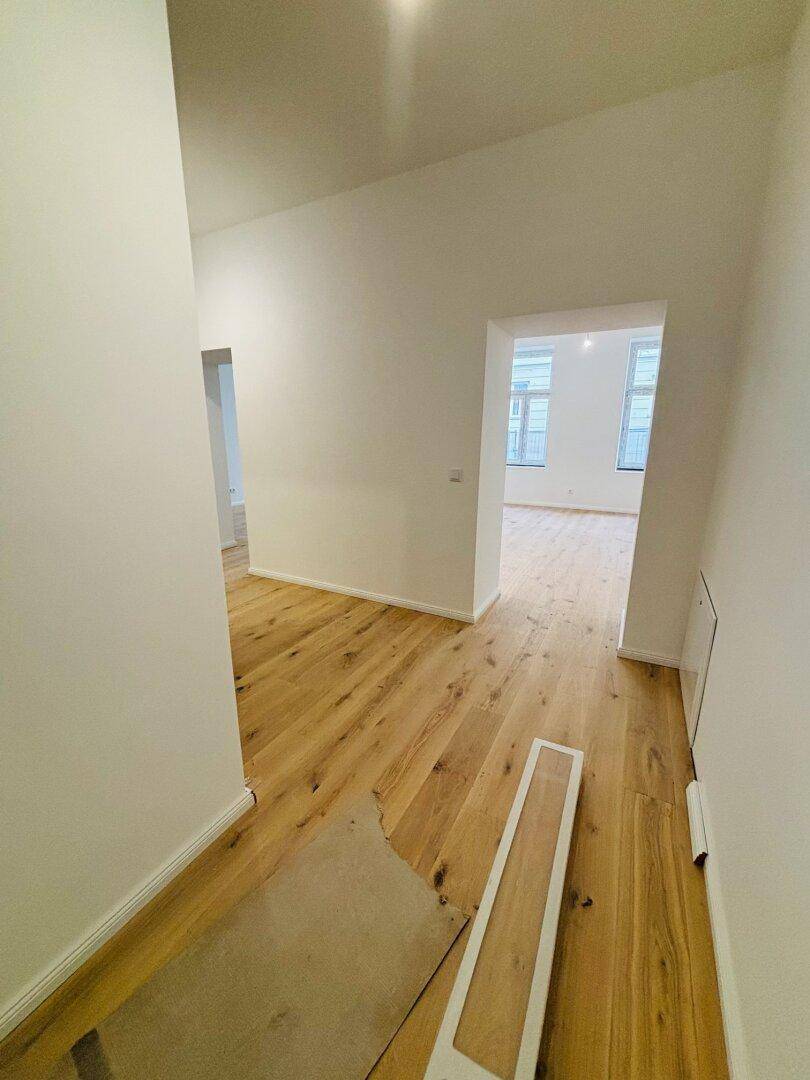 Heller Flur mit neu verlegtem Holzboden und Blick in angrenzende, leere Räume.
