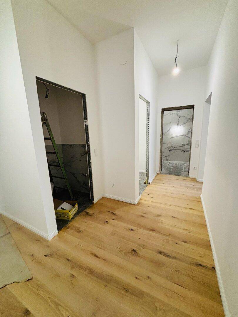 Flur mit Holzboden und offenen Türen zu Räumen in Renovierung, inklusive Leiter.