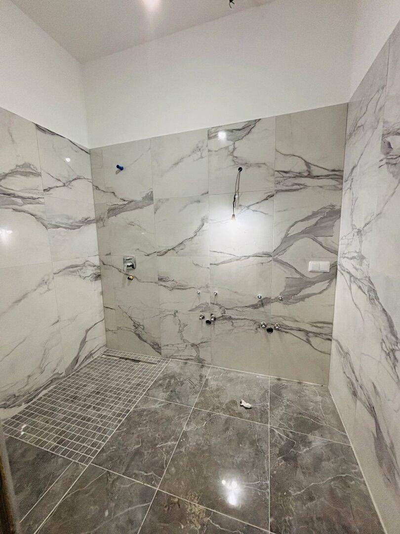 Badezimmer im Bau mit Marmorfliesen an Wänden und Boden, bereit für Installationen.