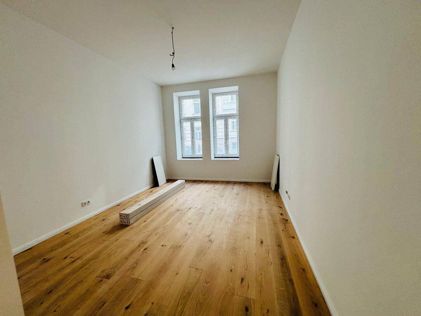 Leeres Schlafzimmer mit neuem Holzboden, hohen Decken und zwei großen Fenstern.