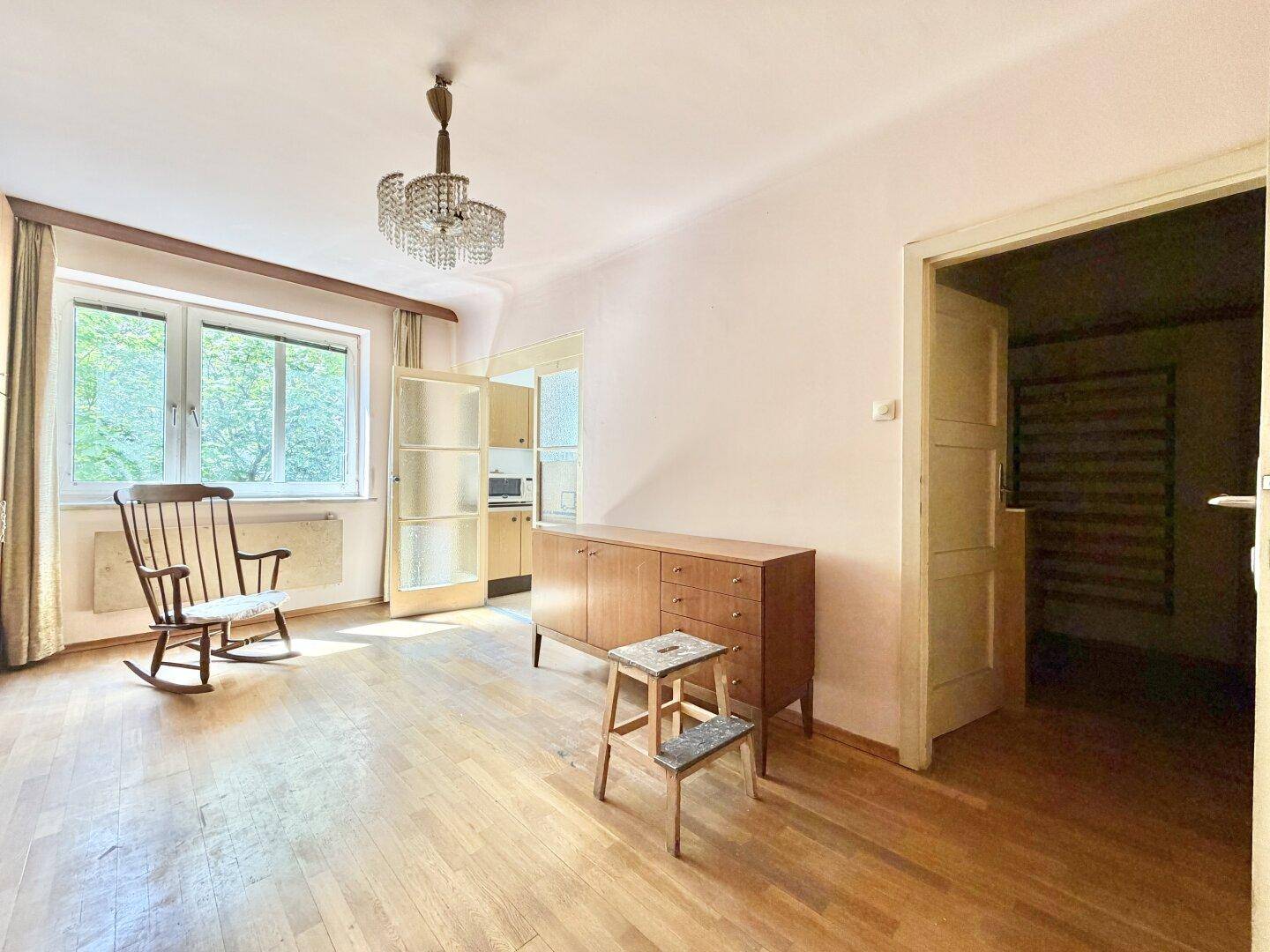 Heller Wohnraum mit Parkettboden, einem Schaukelstuhl und großen Fenstern mit Grünblick.