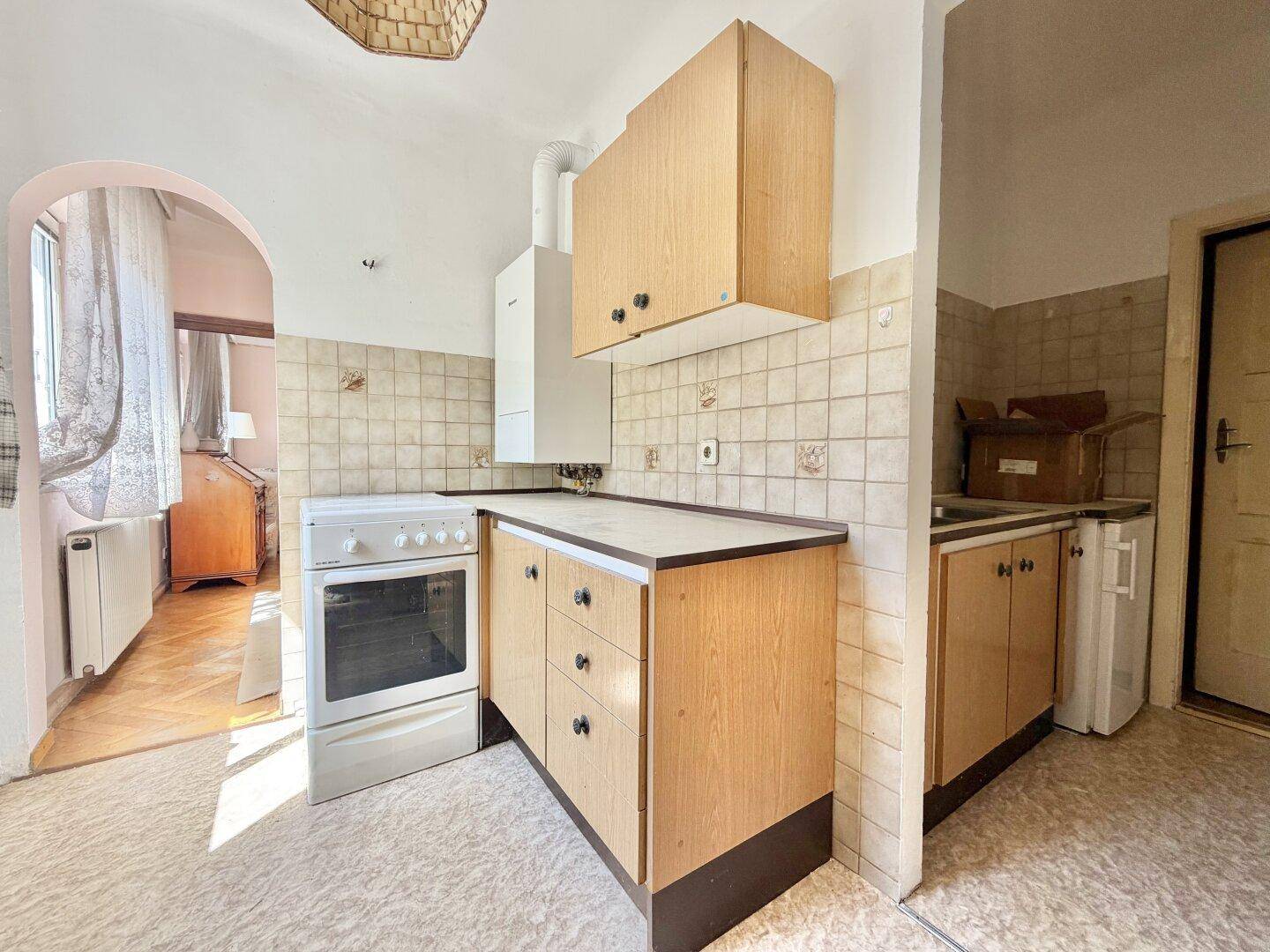 Einfache Küche mit Holzschränken, Fliesenrückwand und einem freistehenden Herd mit Backofen.
