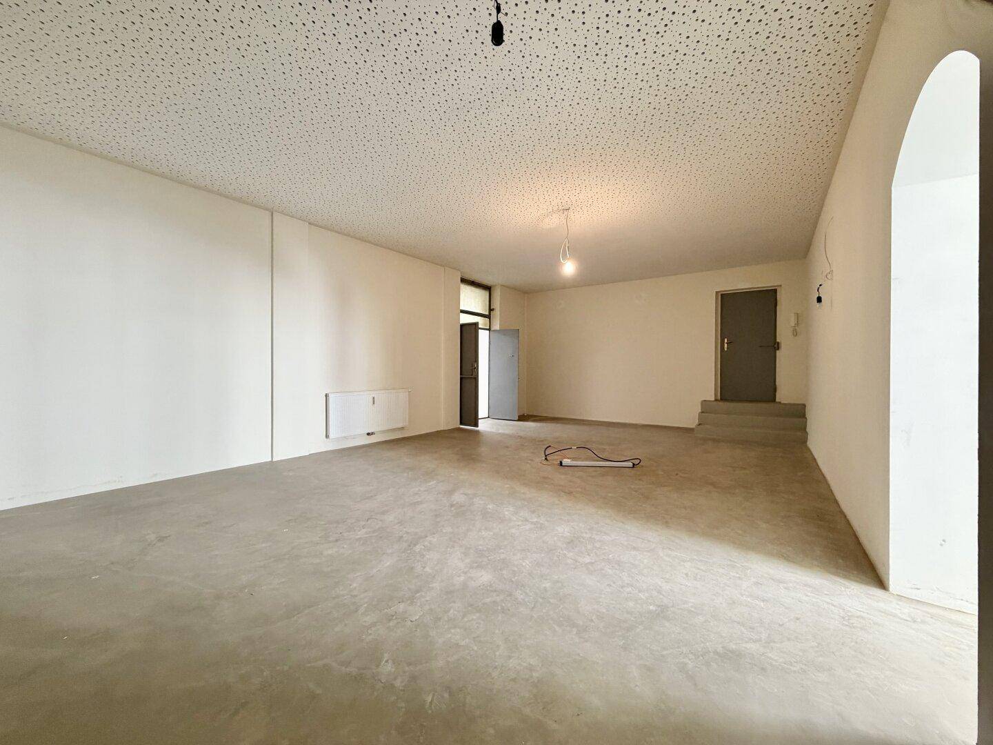 Großer, leerer Gewerberaum mit Betonboden, einer Tür und einer kleinen Stufe im Hintergrund.