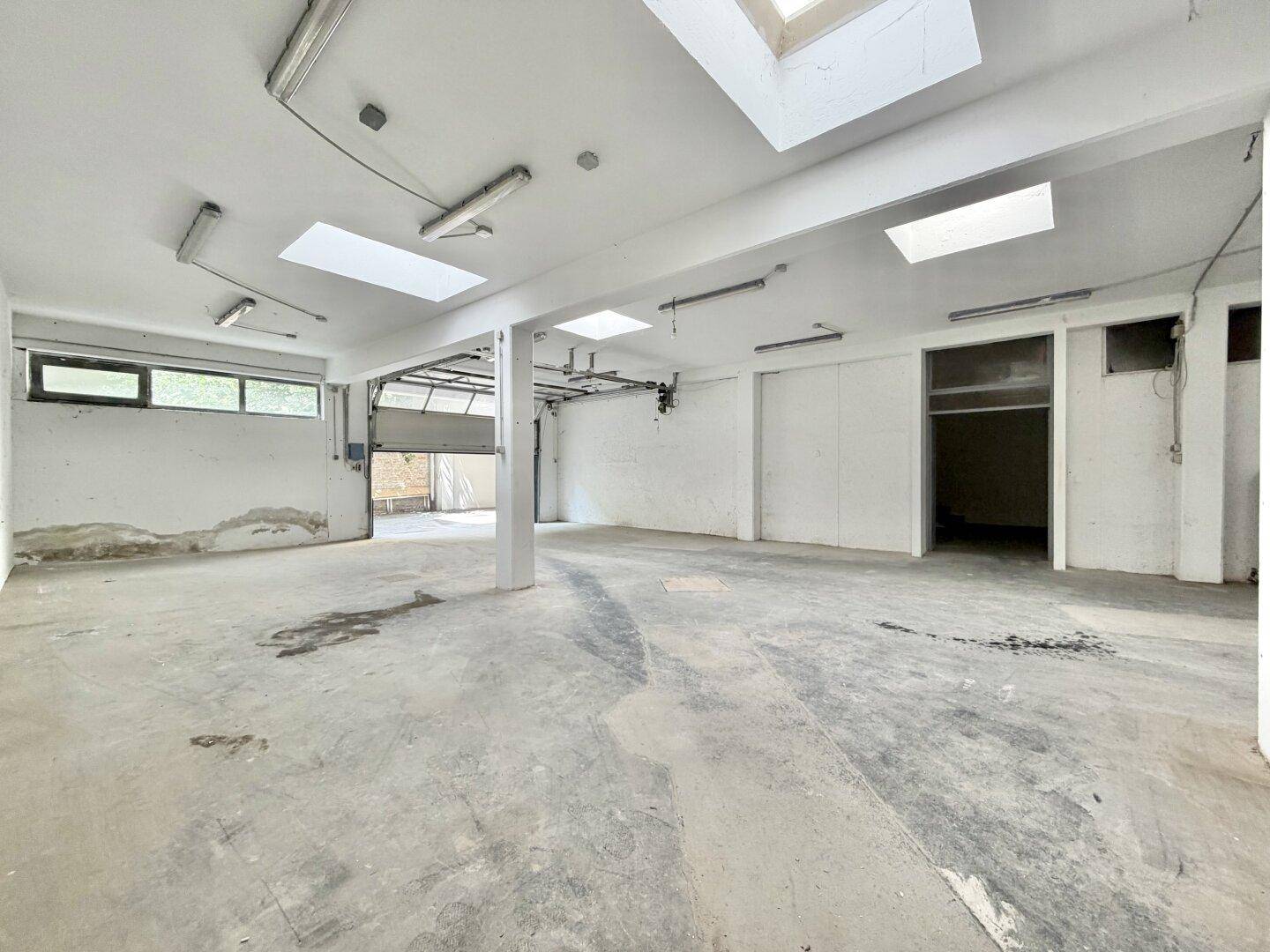 Große Lagerhalle mit Betonboden, Oberlichtern, Fenstern und einem geöffneten Rolltor.