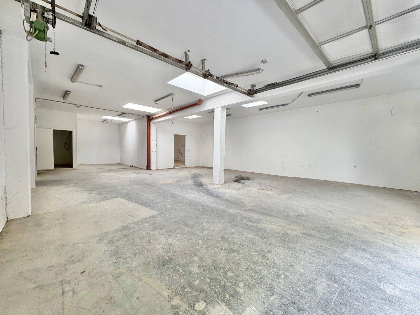 Großer Lagerraum mit Betonboden, Stützpfeiler, Oberlichtern und industrieller Beleuchtung.