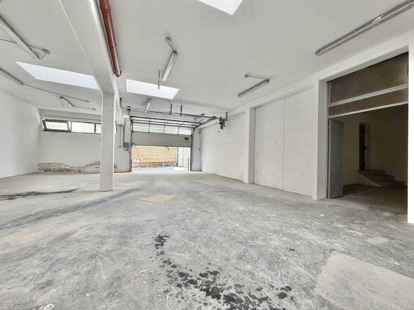 Weitläufige Lagerhalle mit Betonboden, Oberlichtern und einem großen Rolltor am Eingang.