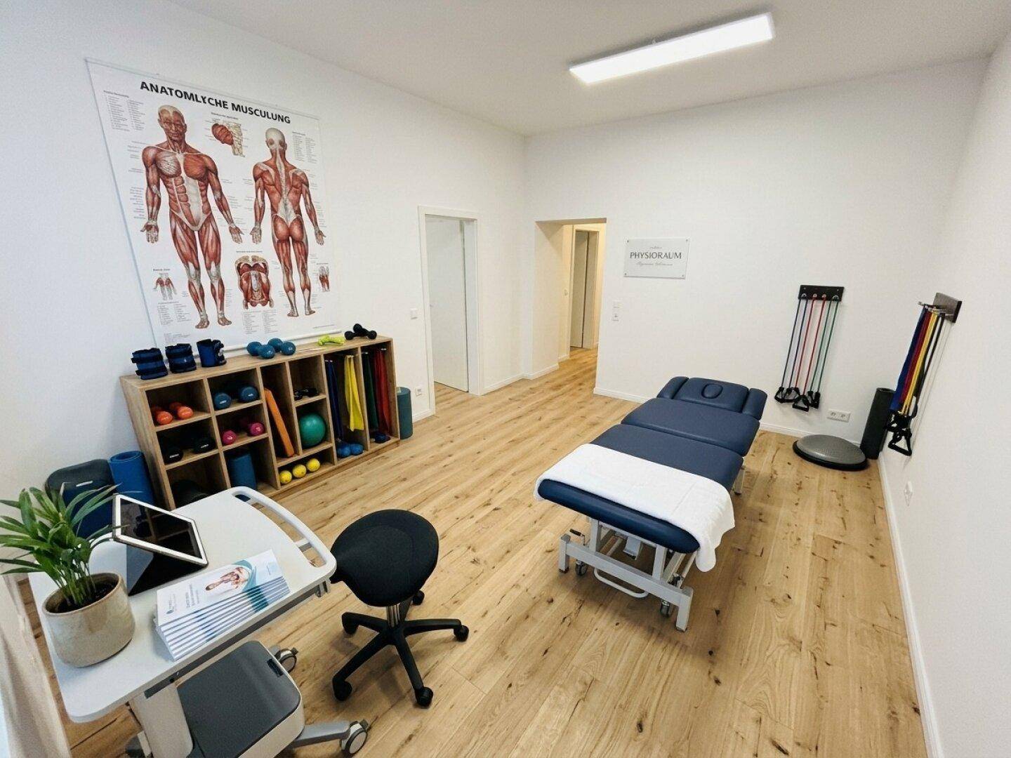 Heller Raum, ausgestattet als Fitness- oder Physiotherapiebereich mit Trainingsgeräten und Holzboden.