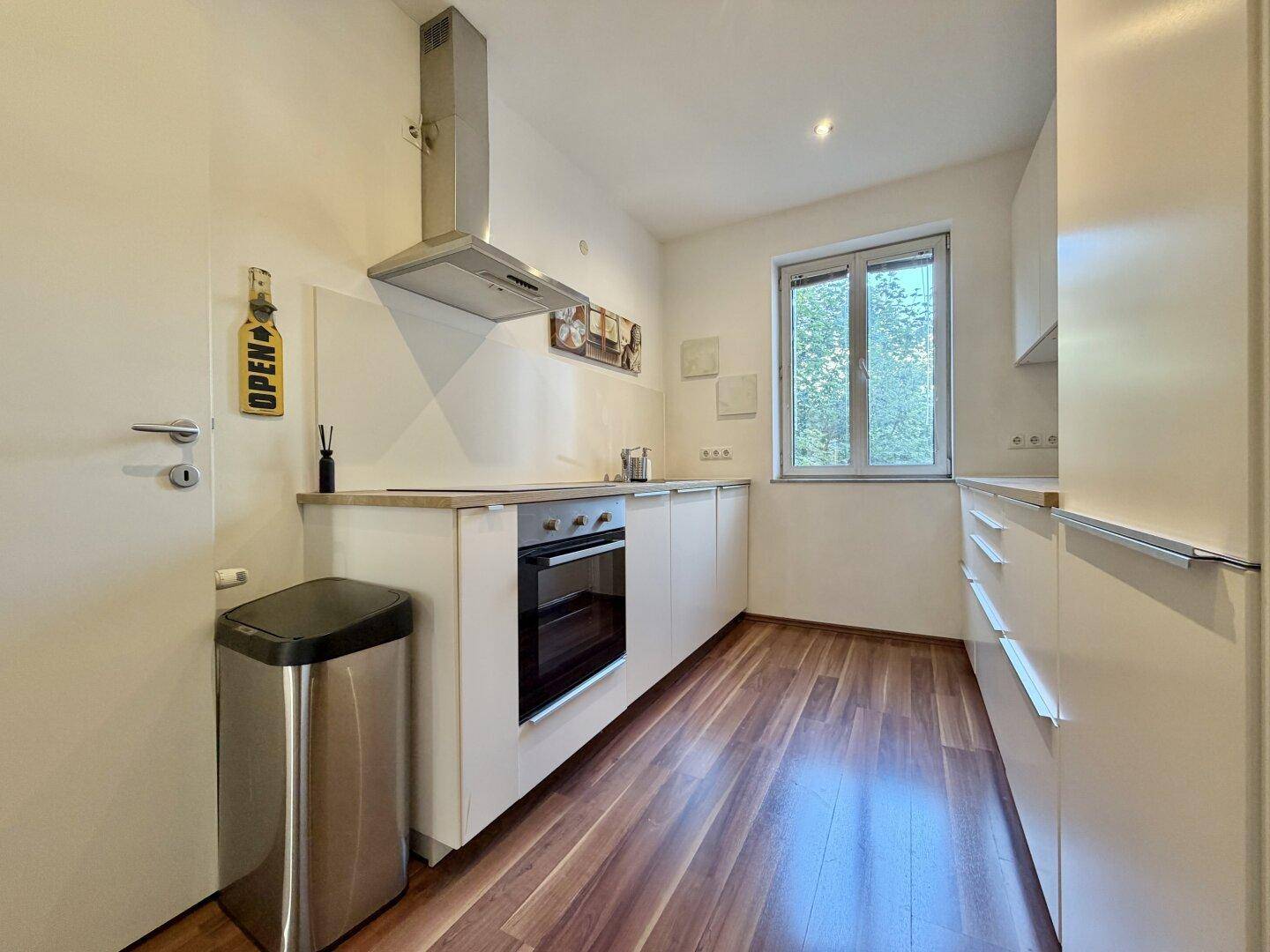 Moderne Einbauküche mit weißen Schränken, Backofen und Dunstabzugshaube, funktional und hell.
