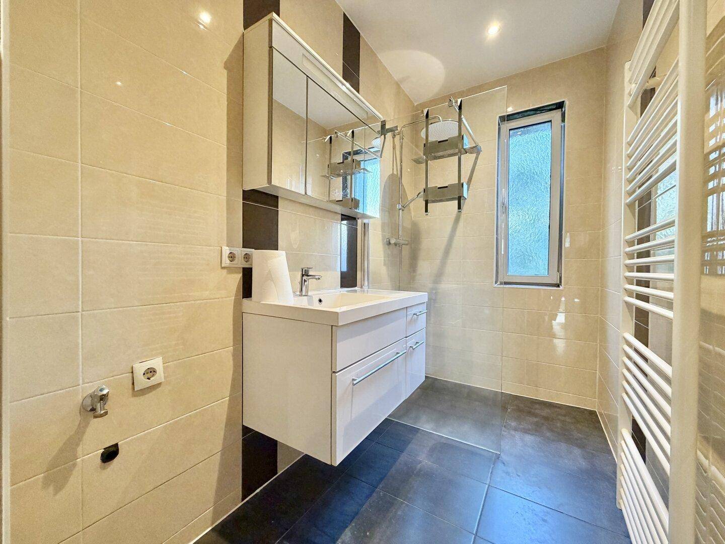 Modernes Badezimmer mit beigen und braunen Fliesen, Waschtisch und Spiegel, gepflegter Zustand.