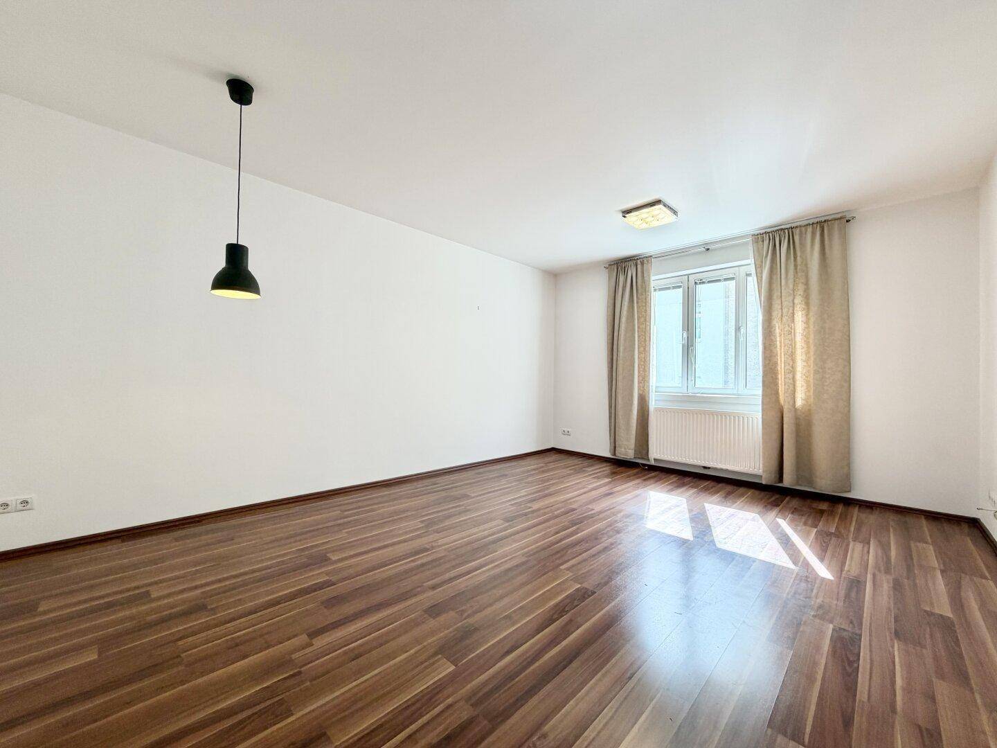 Lichtdurchflutetes Zimmer mit Laminatboden und schlichter Pendelleuchte, einladende Atmosphäre.