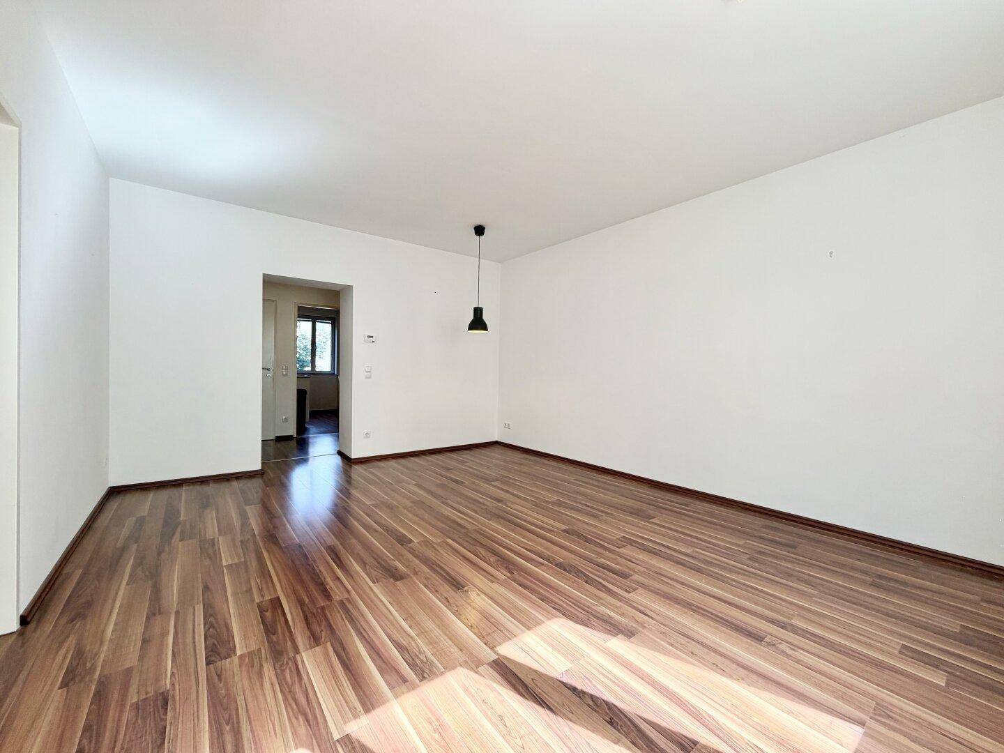 Leeres Zimmer mit Laminatboden und Blick in den Flur, bietet viel Gestaltungspotenzial.