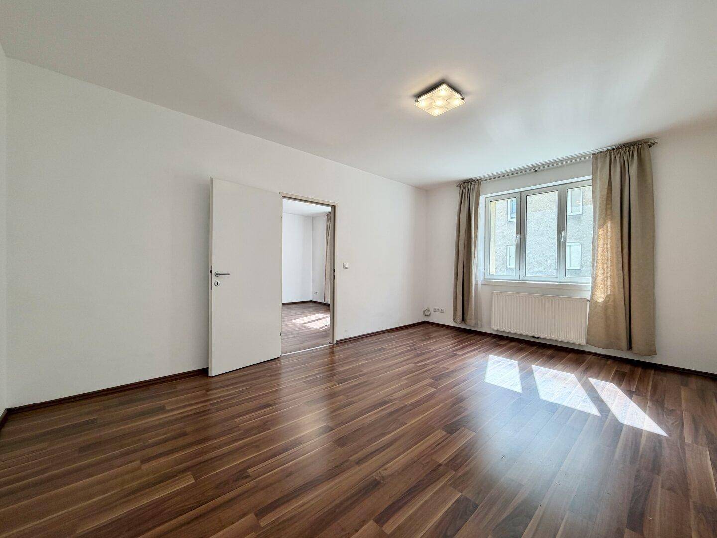 Heller Raum mit Laminatboden und Zugang zu einem weiteren Zimmer, vielseitig nutzbar.