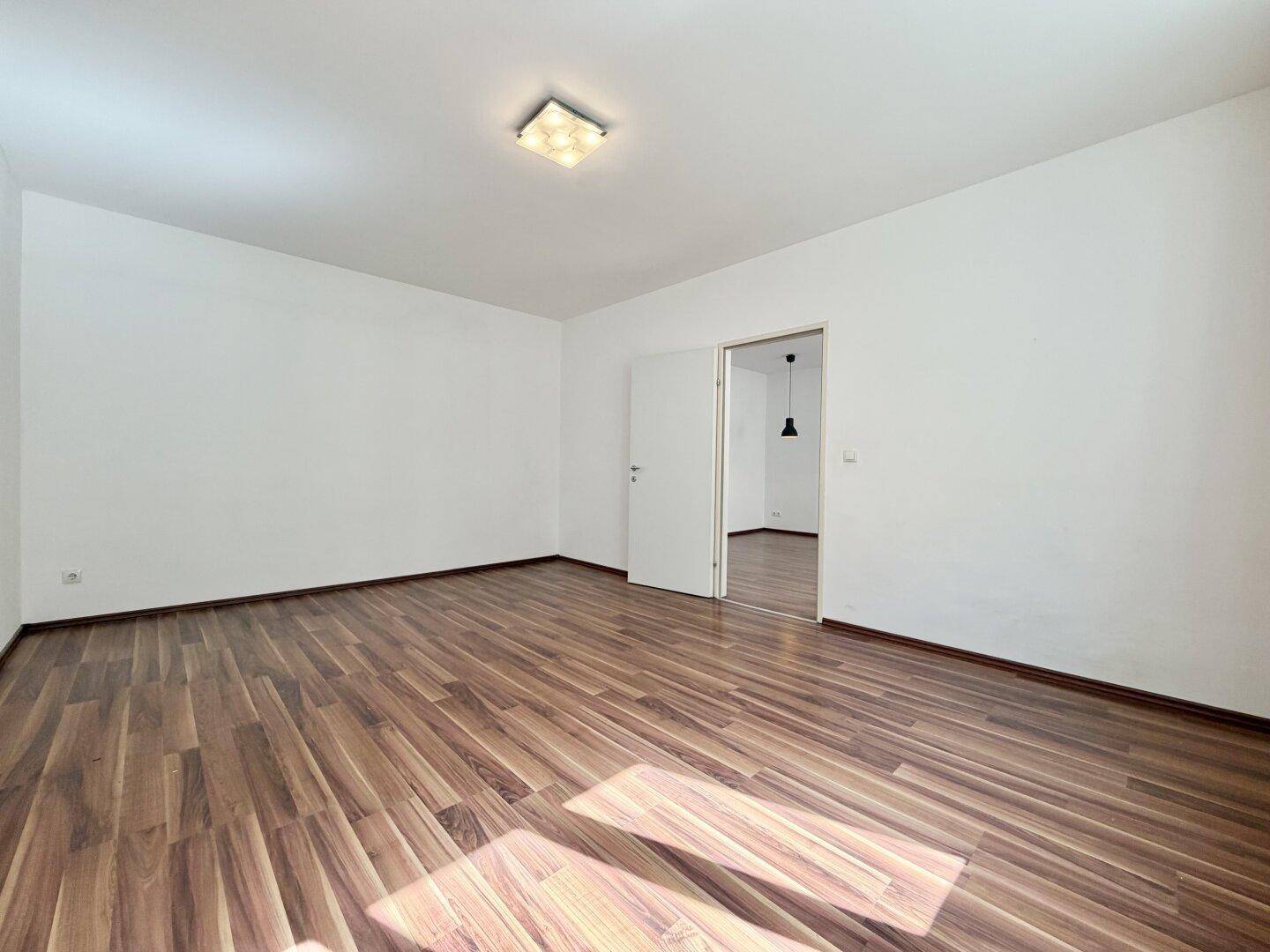Heller Raum mit Laminatboden und offener Tür zu einem angrenzenden Zimmer, gute Raumaufteilung.