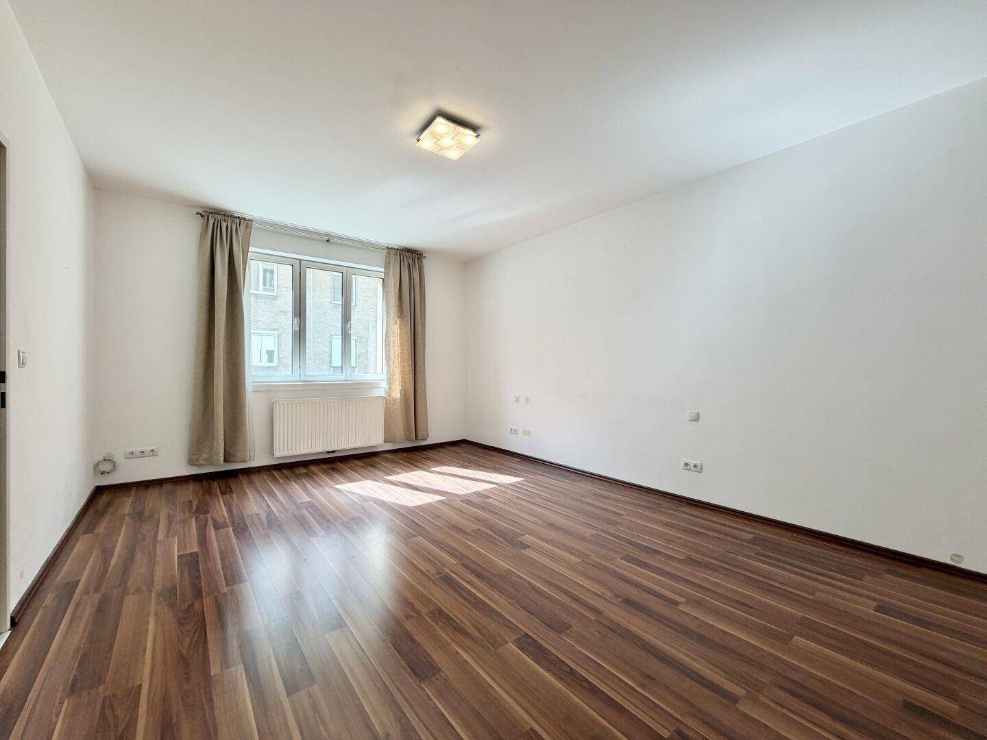 Geräumiges Zimmer mit Laminatboden, Fenster und Heizkörper, angenehmes Wohnklima.