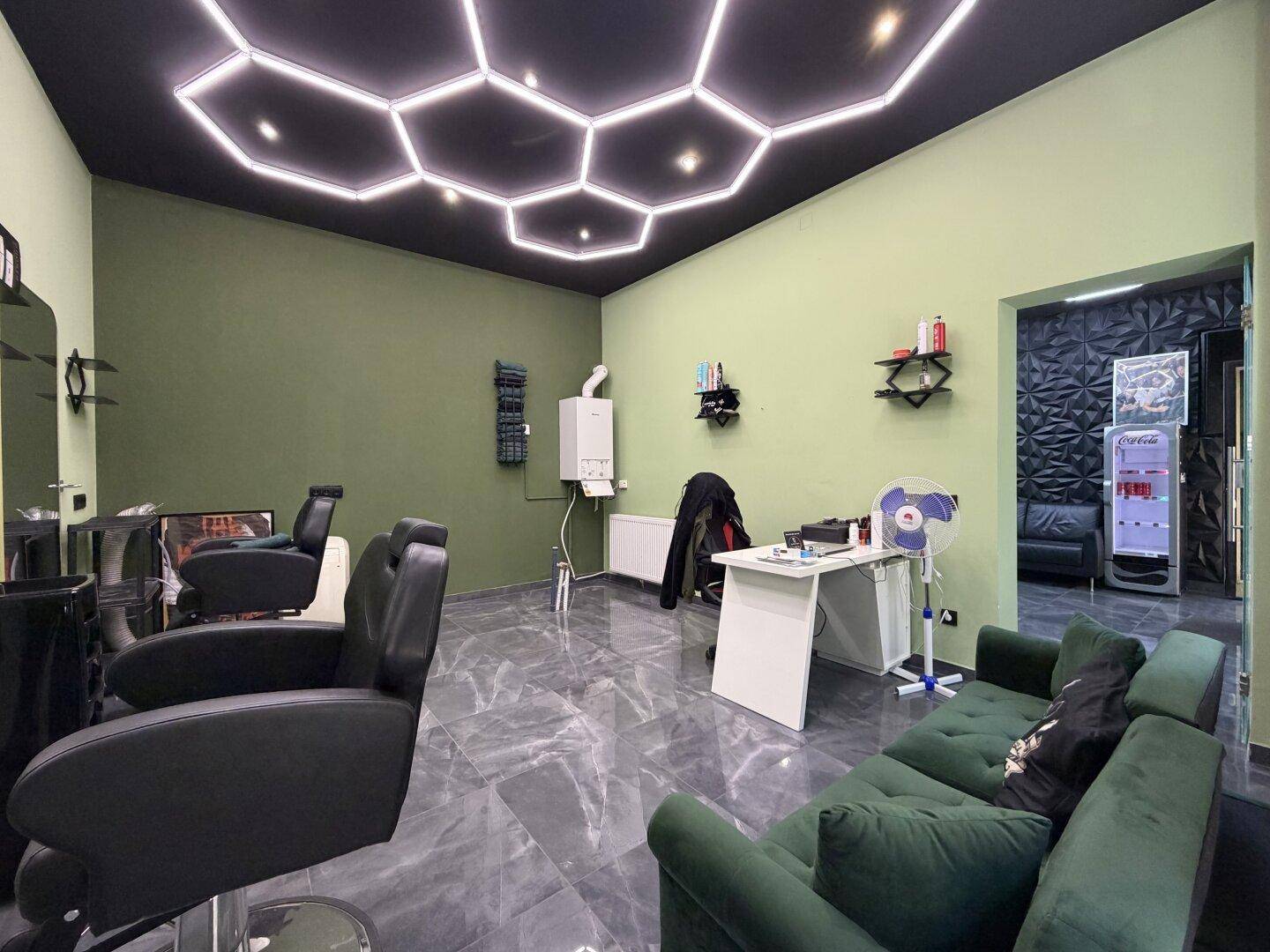 Geräumiger Friseursalon mit grünen Wänden, dunklen Fliesen und einer modernen Sitzgelegenheit für Kunden.
