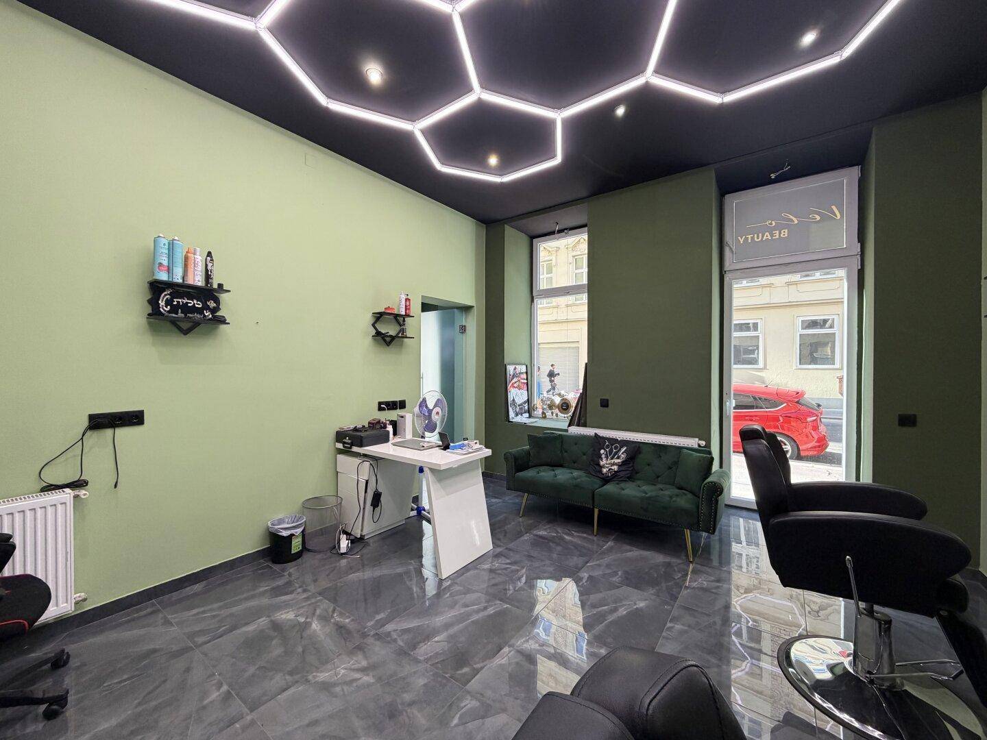 Heller Friseursalon mit grünen Wänden, dunklem Boden und einem Wartebereich mit bequemen Sofas.