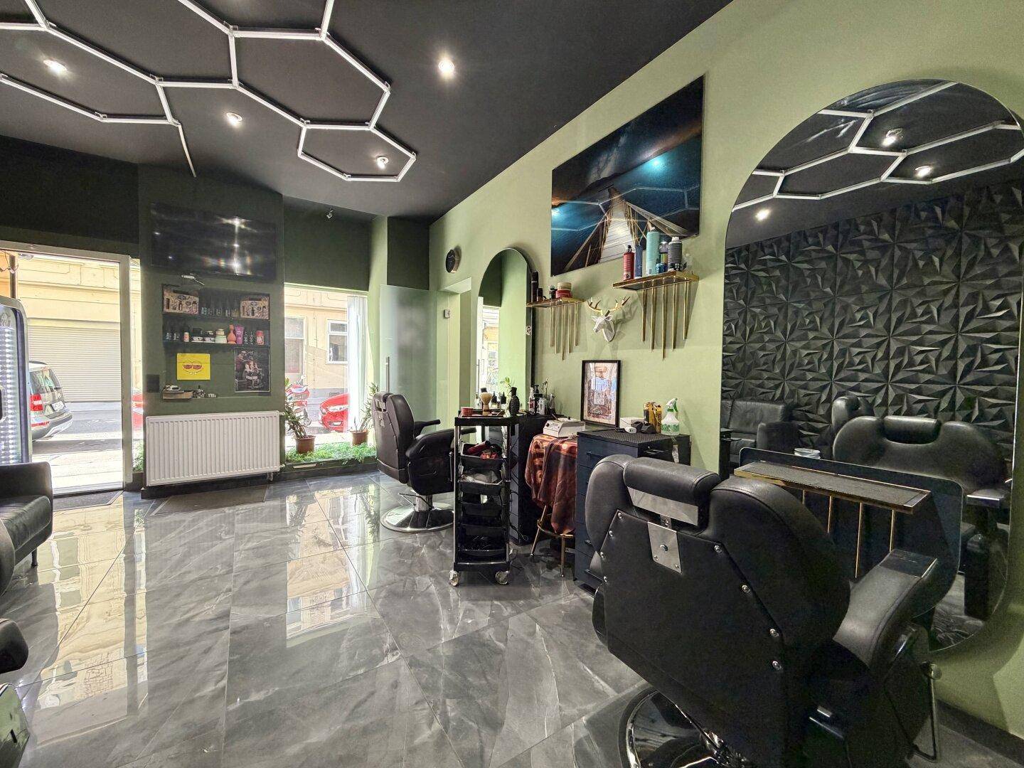 Heller Friseursalon mit großen Fenstern zur Straße, modernen Spiegeln und stilvoller Wabenbeleuchtung an der Decke.