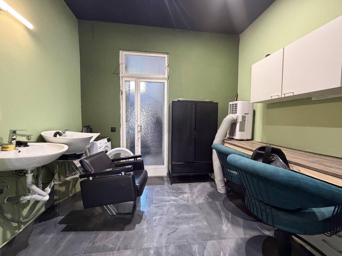 Waschbereich im Friseursalon mit zwei Waschbecken, dunklen Fliesen und einem Fenster zur Belüftung.