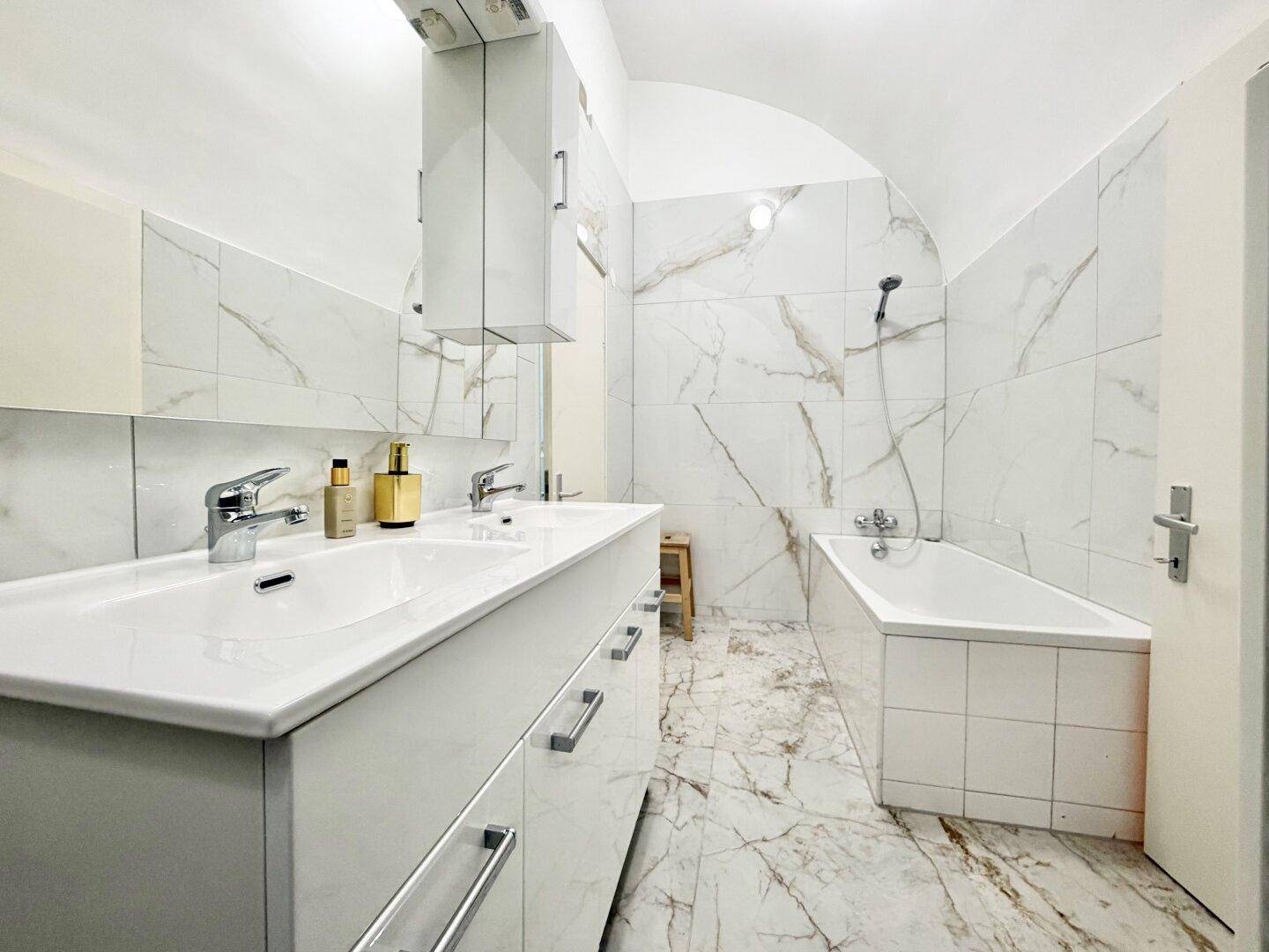 Modernes Badezimmer mit Doppelwaschbecken, Badewanne und eleganten Marmorfliesen an Wänden und Boden.