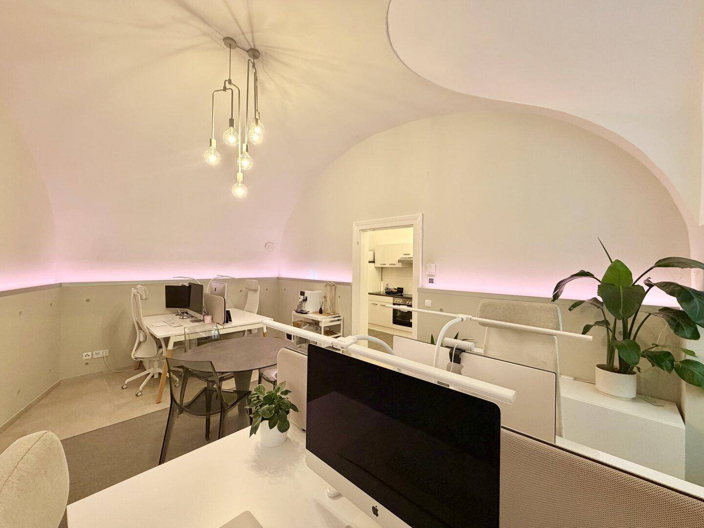 Geräumiges Büro mit moderner Einrichtung, gewölbter Decke und Zugang zu einer kleinen Küche.