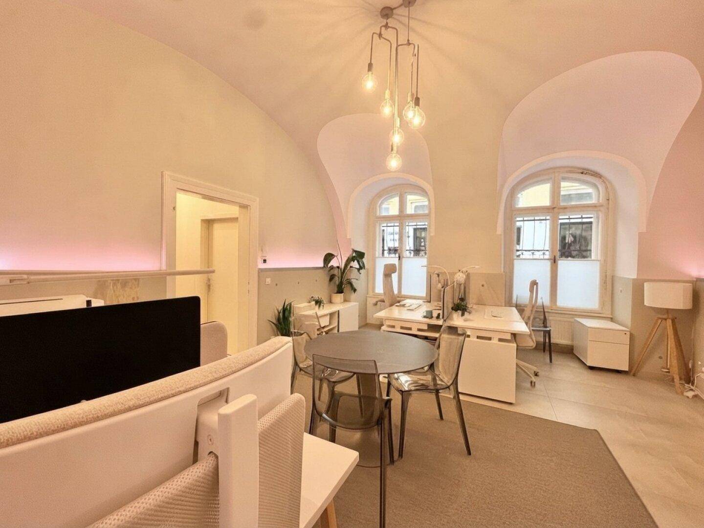 Helles Büro mit mehreren Arbeitsplätzen, modernen Möbeln und charakteristischen Bogenfenstern.