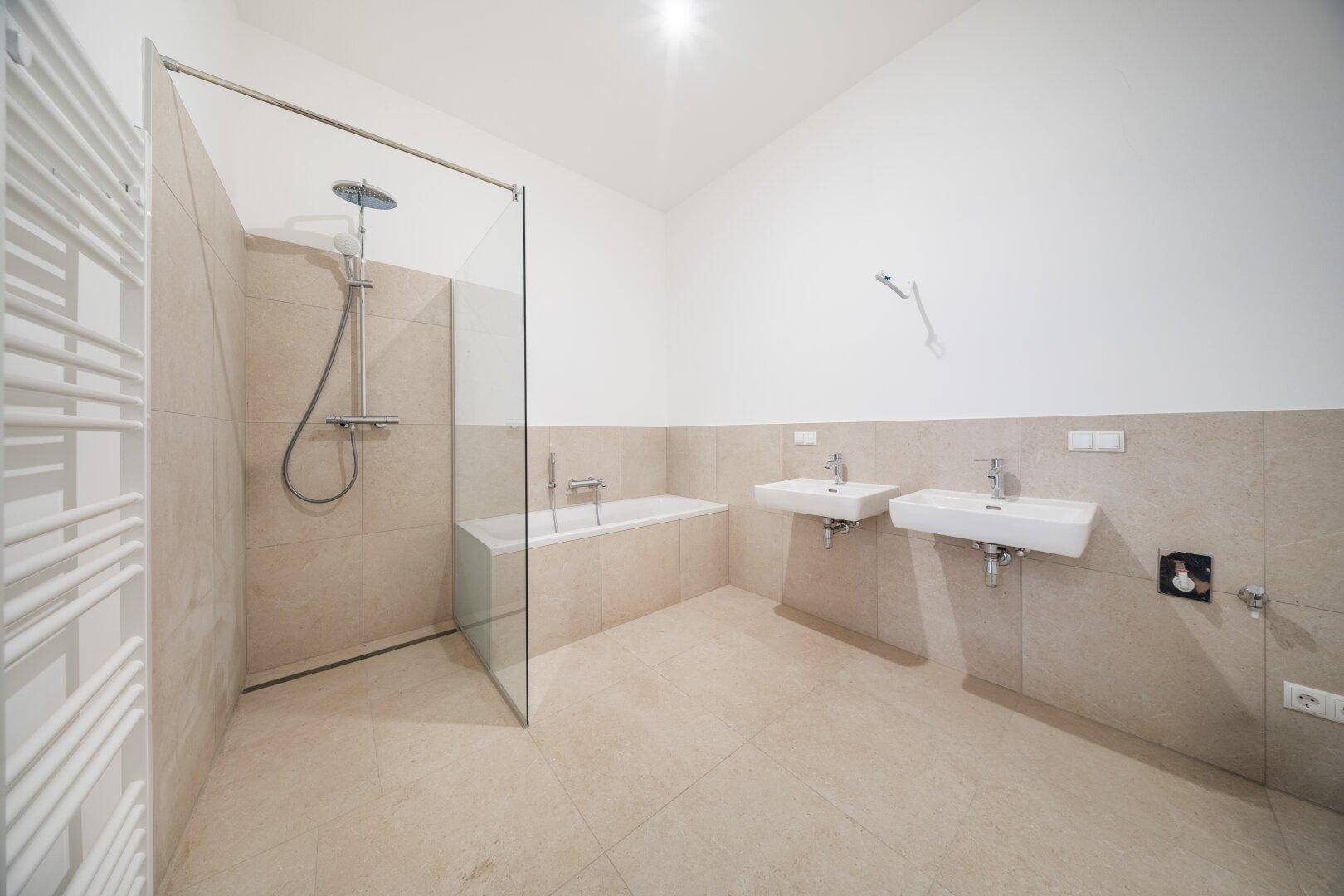 Modernes Badezimmer mit beigen Fliesen, zwei Waschbecken, Badewanne und begehbarer Dusche.