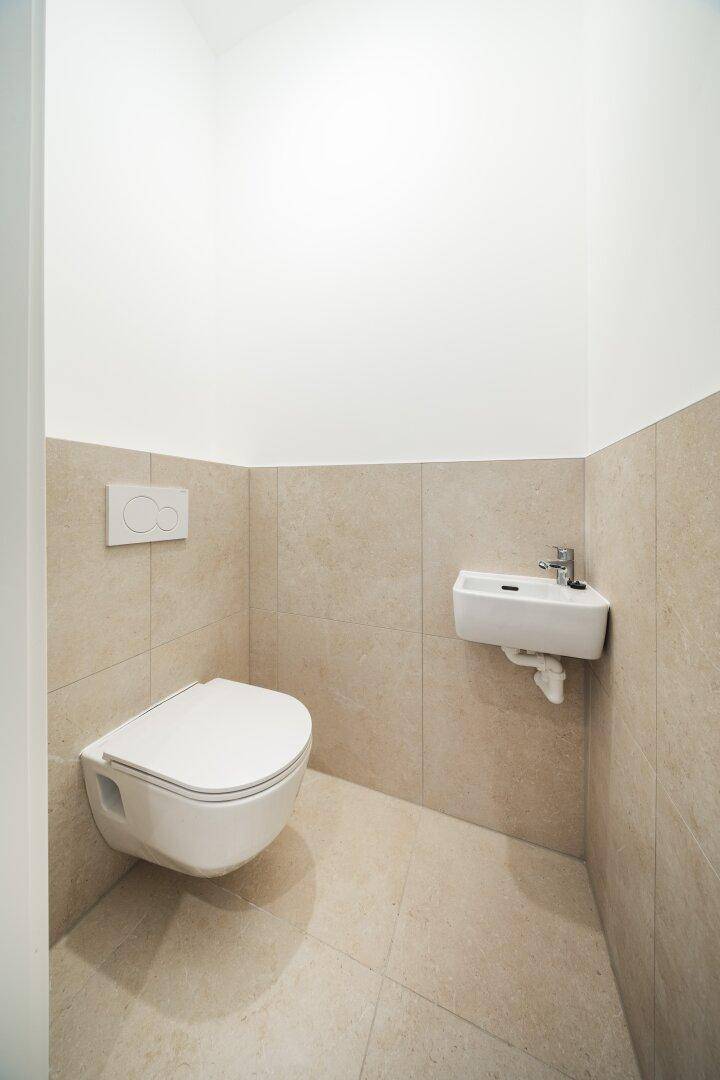 Modernes Gäste-WC mit beigen Fliesen, wandhängendem WC und kleinem Waschbecken.