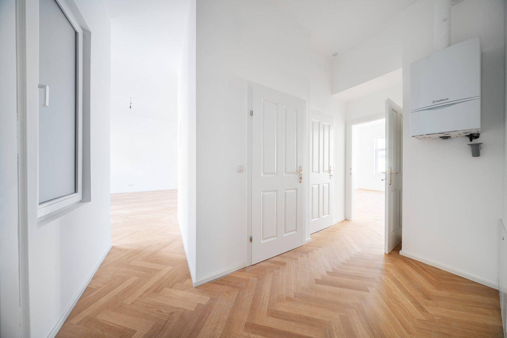 Heller Flur mit Fischgrätparkett, weißen Türen und einem Wandheizkessel, frisch renoviert.