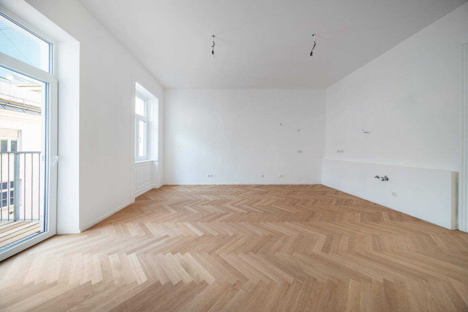Lichtdurchfluteter Raum mit neuem Fischgrätparkett und vorbereiteten Anschlüssen an der Wand.