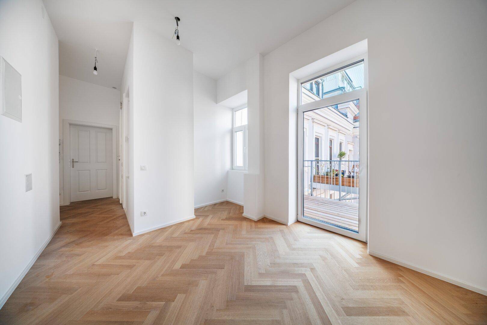 Geräumiges, helles Zimmer mit Fischgrätparkett und Balkonzugang, bereit zur individuellen Gestaltung.