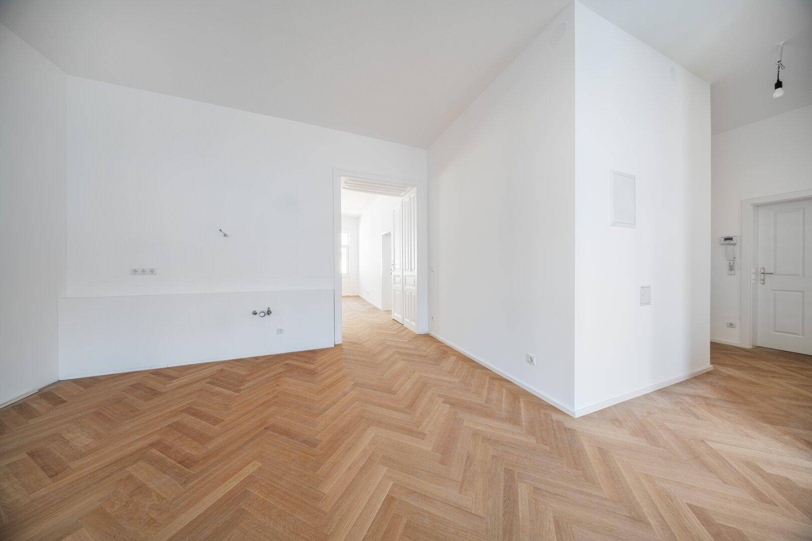 Leeres Zimmer mit Fischgrätparkett und offenem Durchgang zu weiteren Räumen, vielseitig nutzbar.