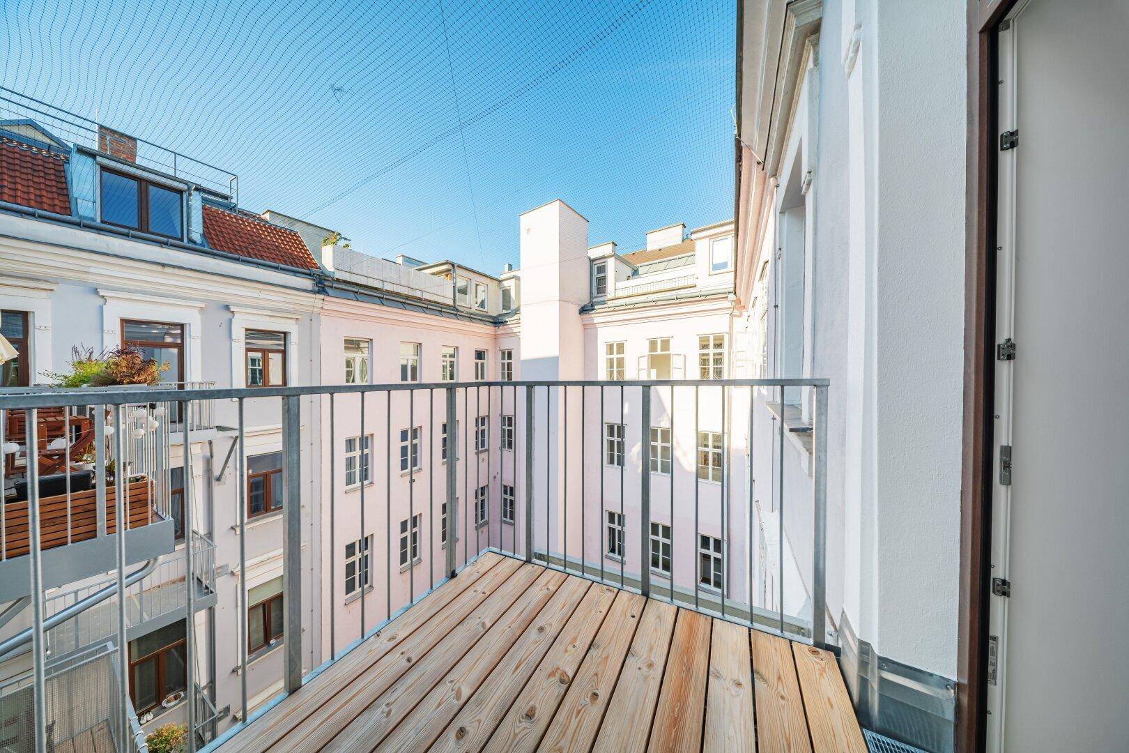 Balkon mit Holzbelag und weitem Blick über den Innenhof der Wohnanlage, sonnig und hell.