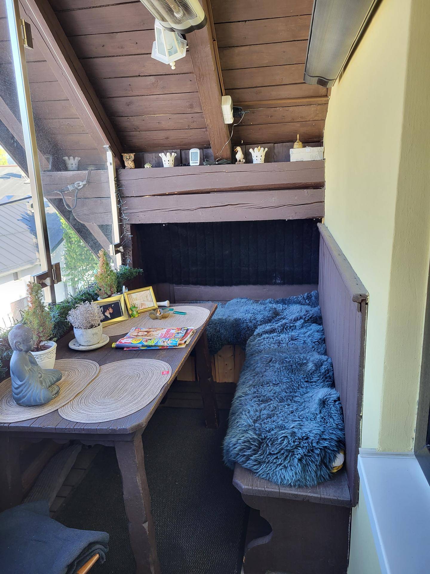 Gemütliche Loggia mit Holztisch und Sitzbank, dekoriert mit Fellen und Pflanzen.