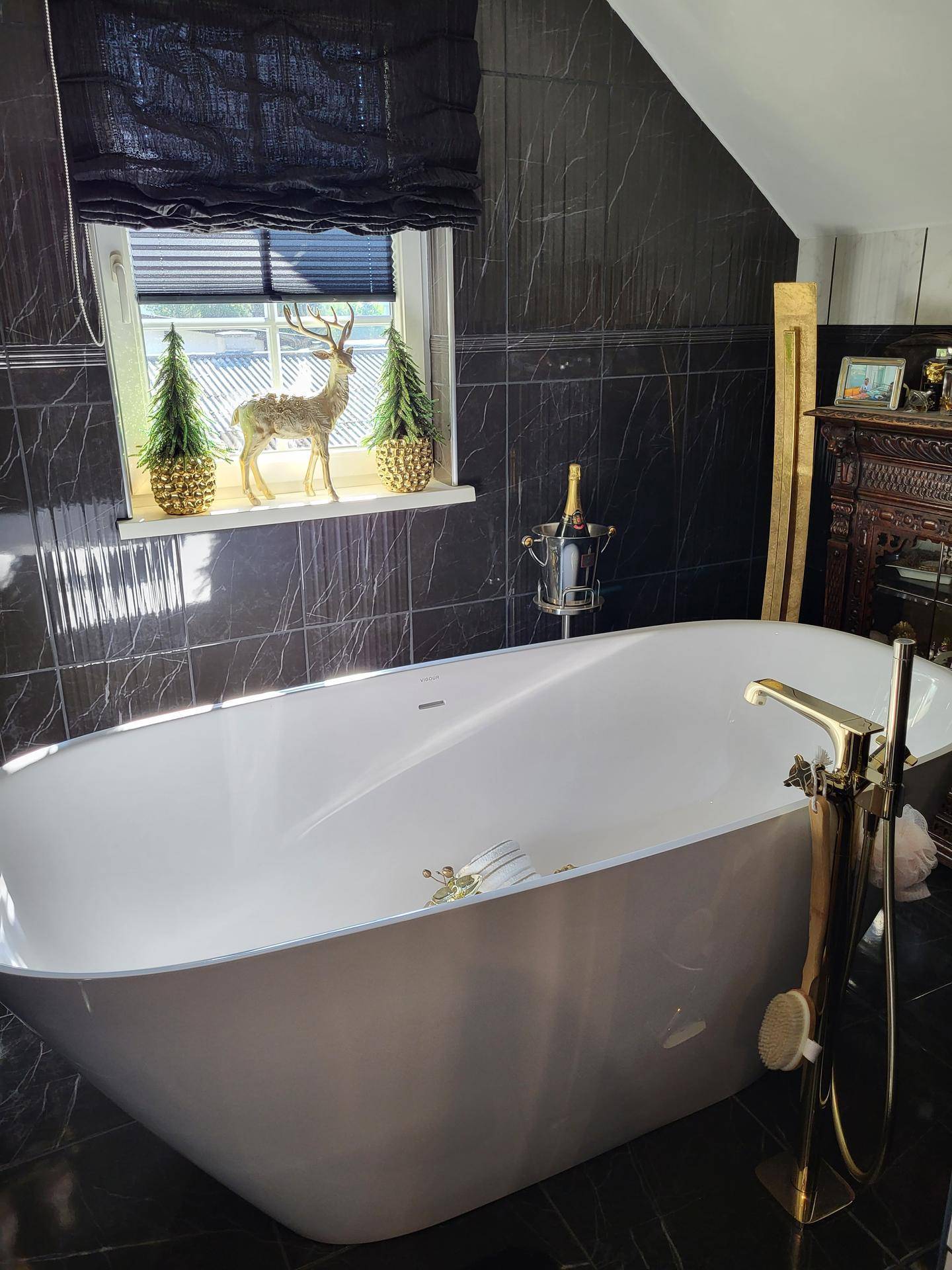 Luxuriöses Badezimmer mit freistehender Badewanne, schwarzen Marmorfliesen und goldenen Armaturen.