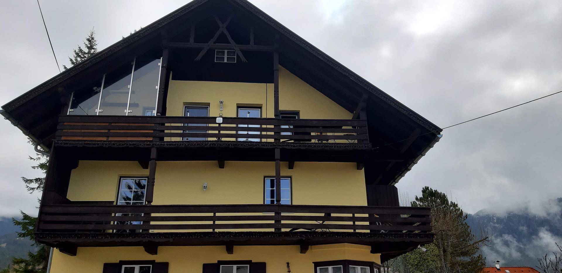Traditionelles Haus mit gelber Fassade, Holzbalkonen und Blick auf die Berge.