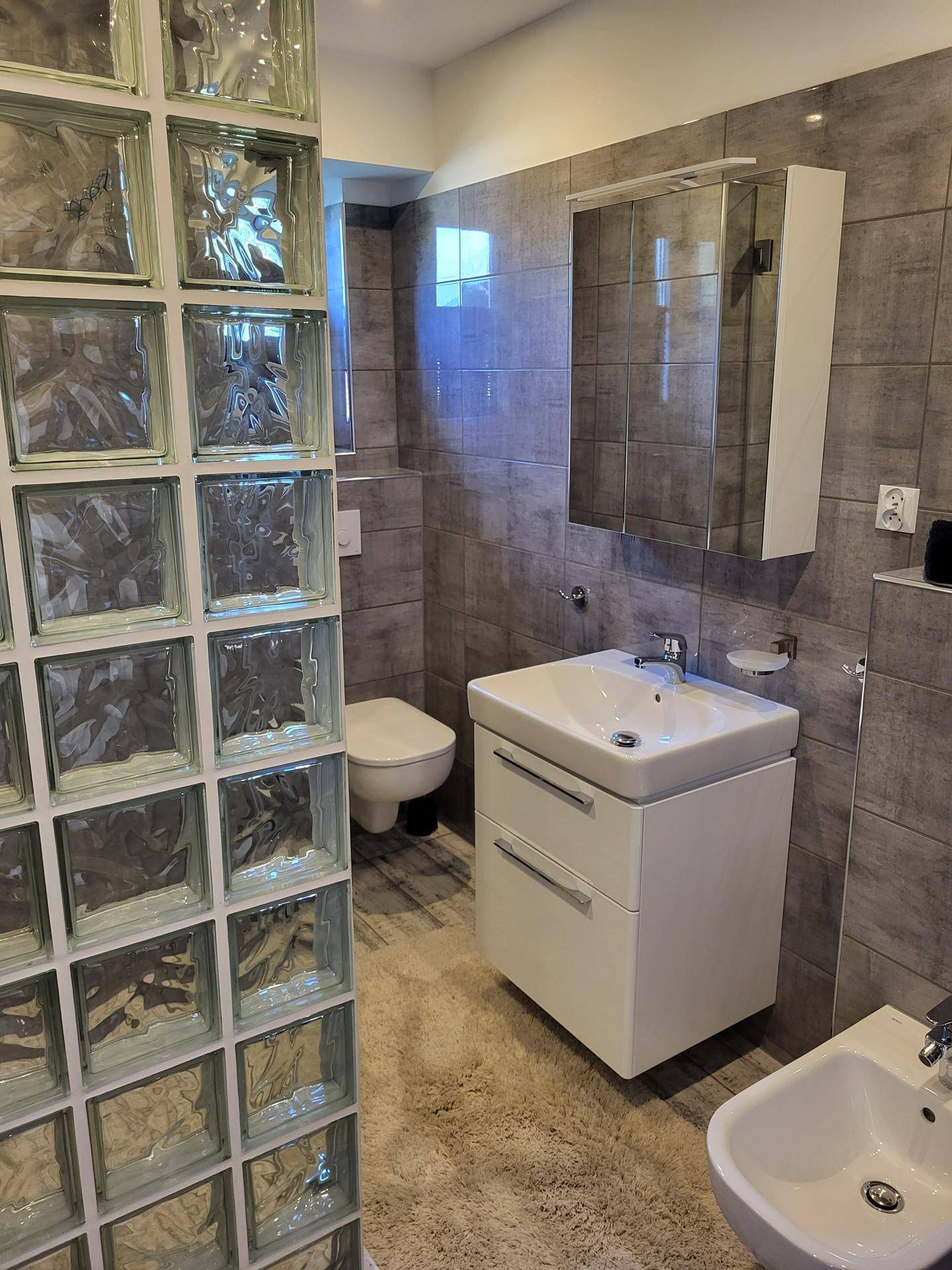 Modernes Badezimmer mit grauen Fliesen, Waschtisch, Hänge-WC und Bidet.
