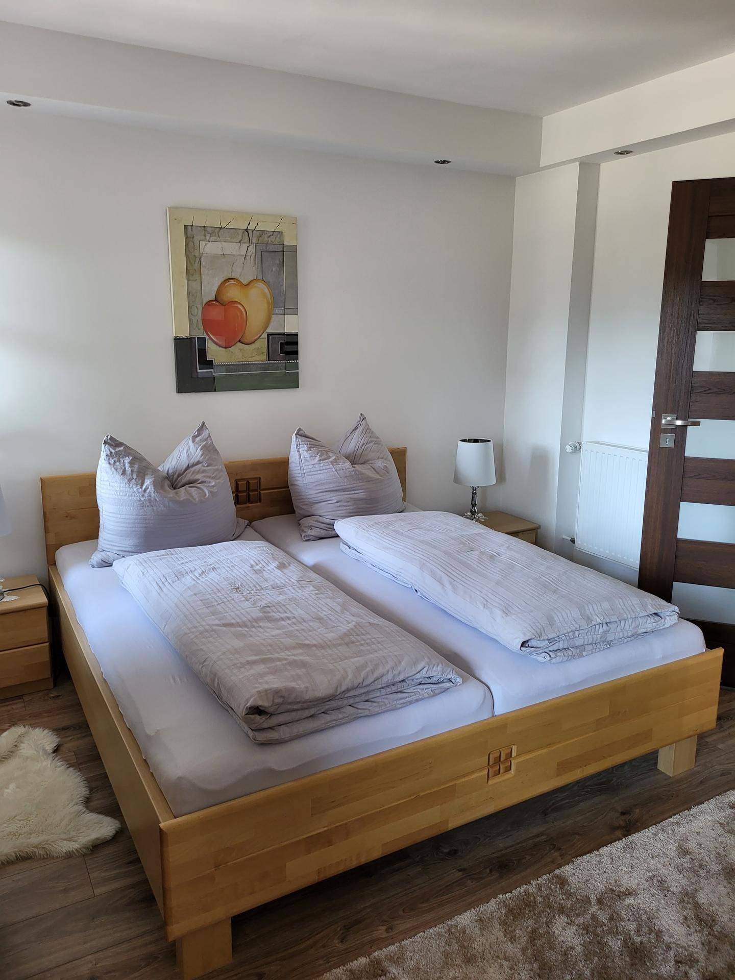 Helles Schlafzimmer mit Doppelbett, Holzboden und moderner Kunst an der Wand.