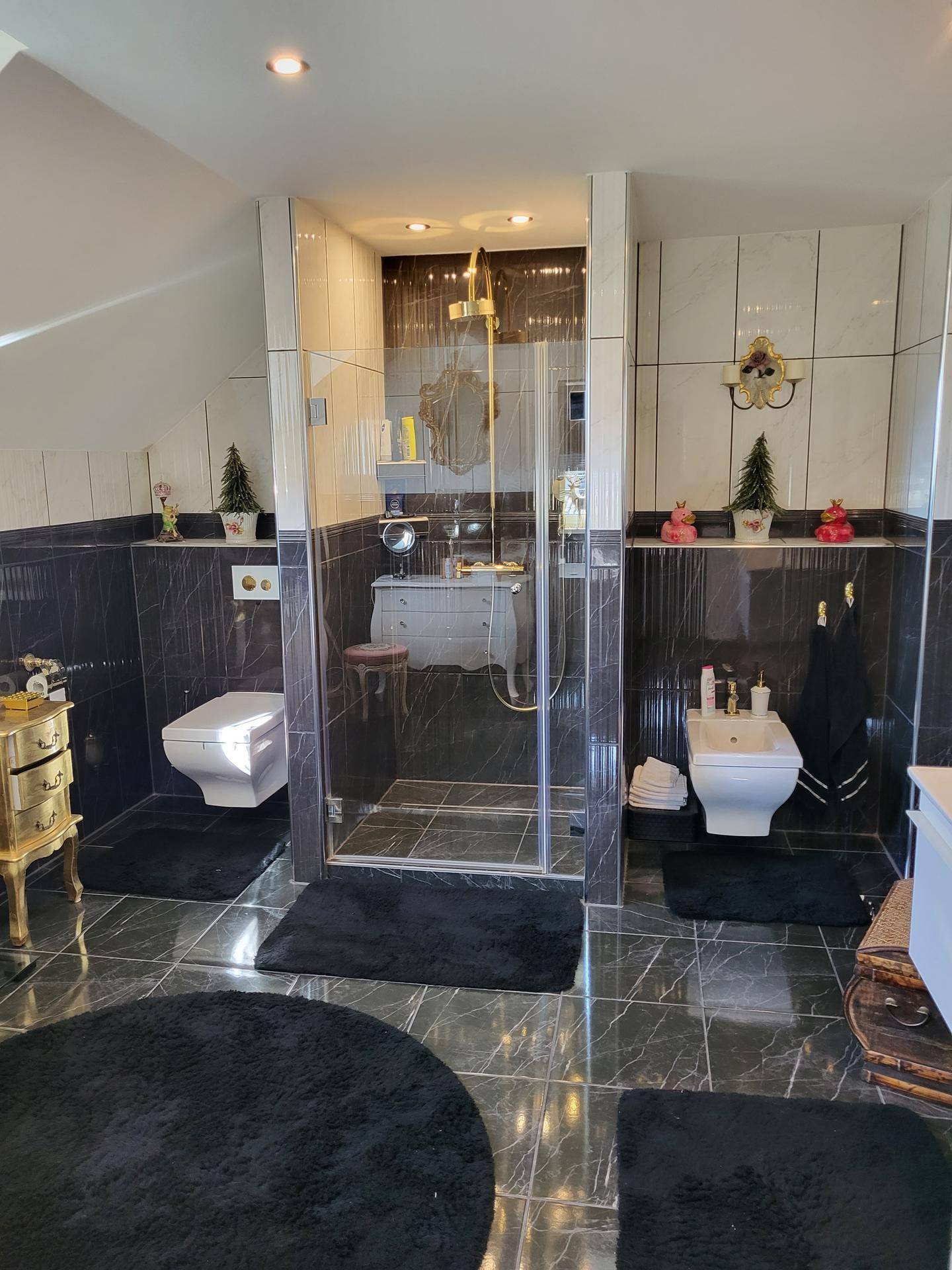 Luxuriöses Badezimmer mit schwarzen Marmorfliesen, Duschkabine und Bidet.