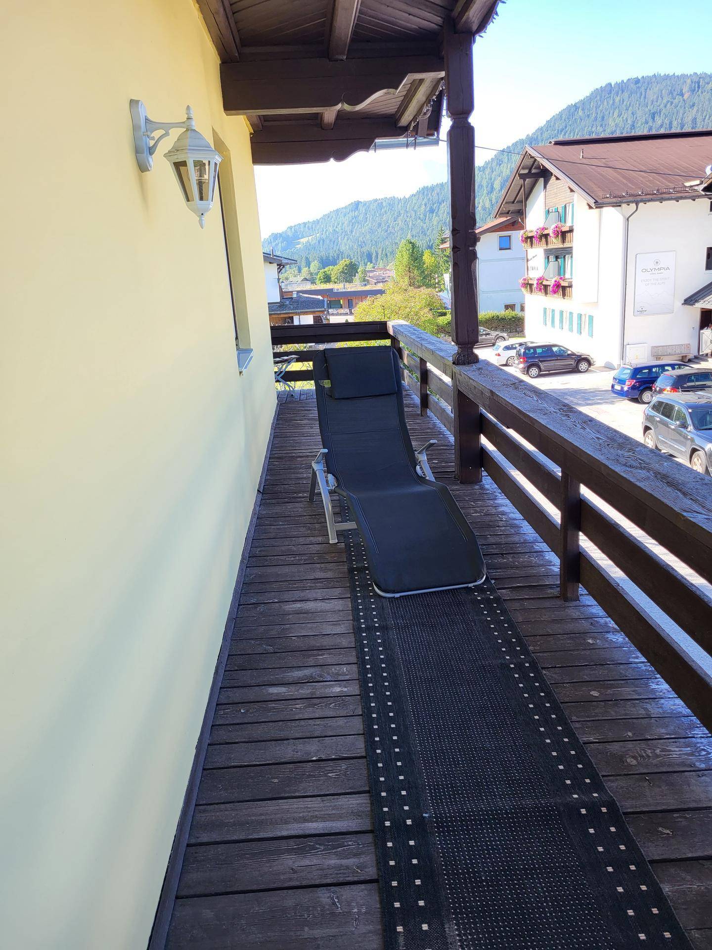 Sonnenbalkon mit Liegestuhl und Blick auf die umliegende Berglandschaft und Häuser.