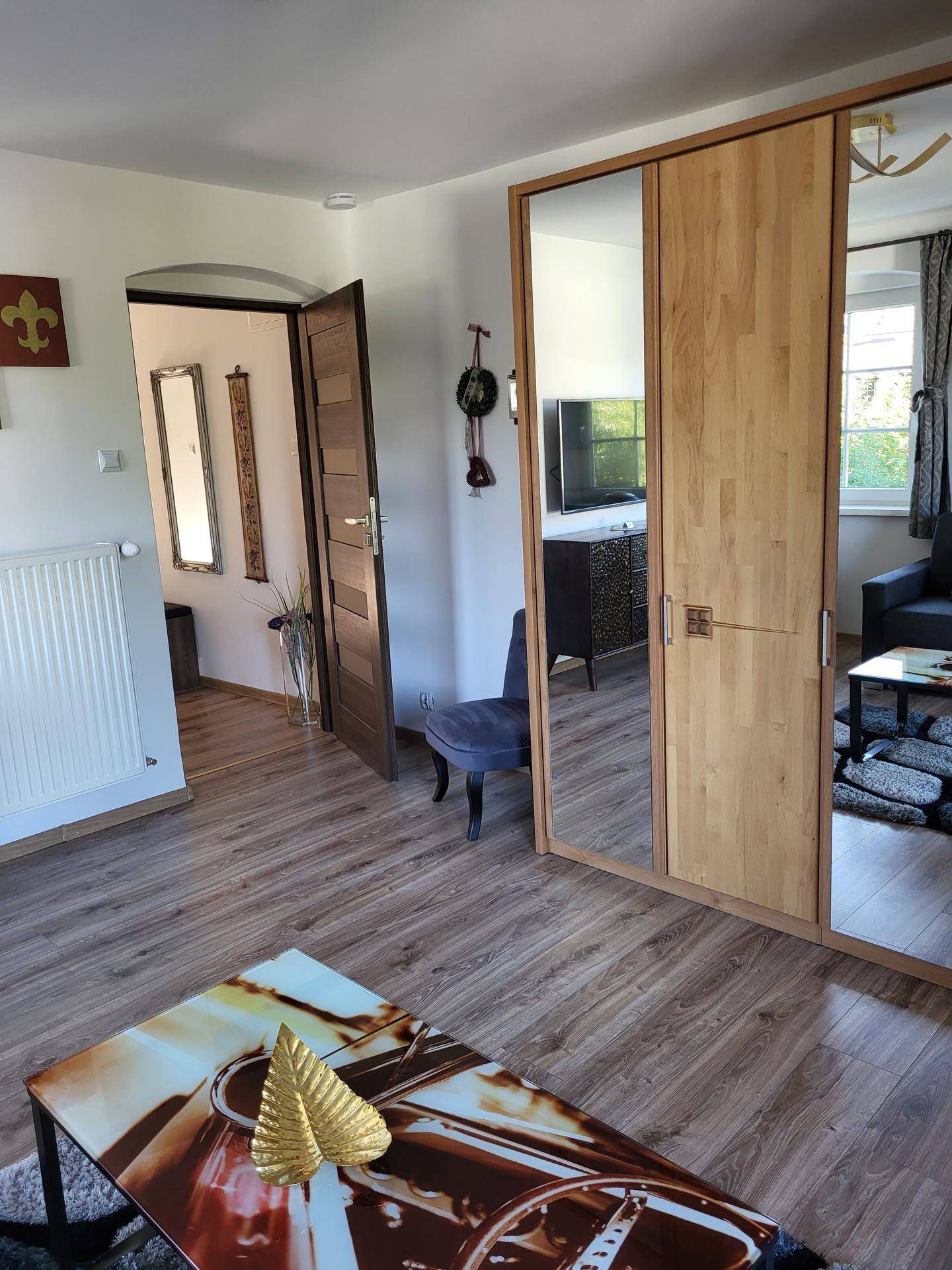 Helles Wohnzimmer mit Holzboden, großem Spiegelschrank und Zugang zum Flur.