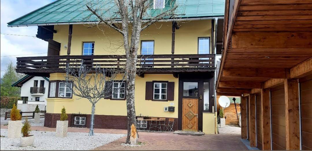 Seitenansicht des gelben Hauses mit Holzbalkonen und einem angrenzenden Carport.