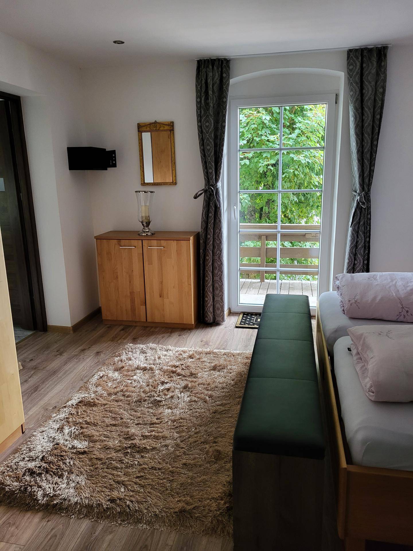 Helles Schlafzimmer mit zwei Einzelbetten, Holzboden und Zugang zu einem Balkon.