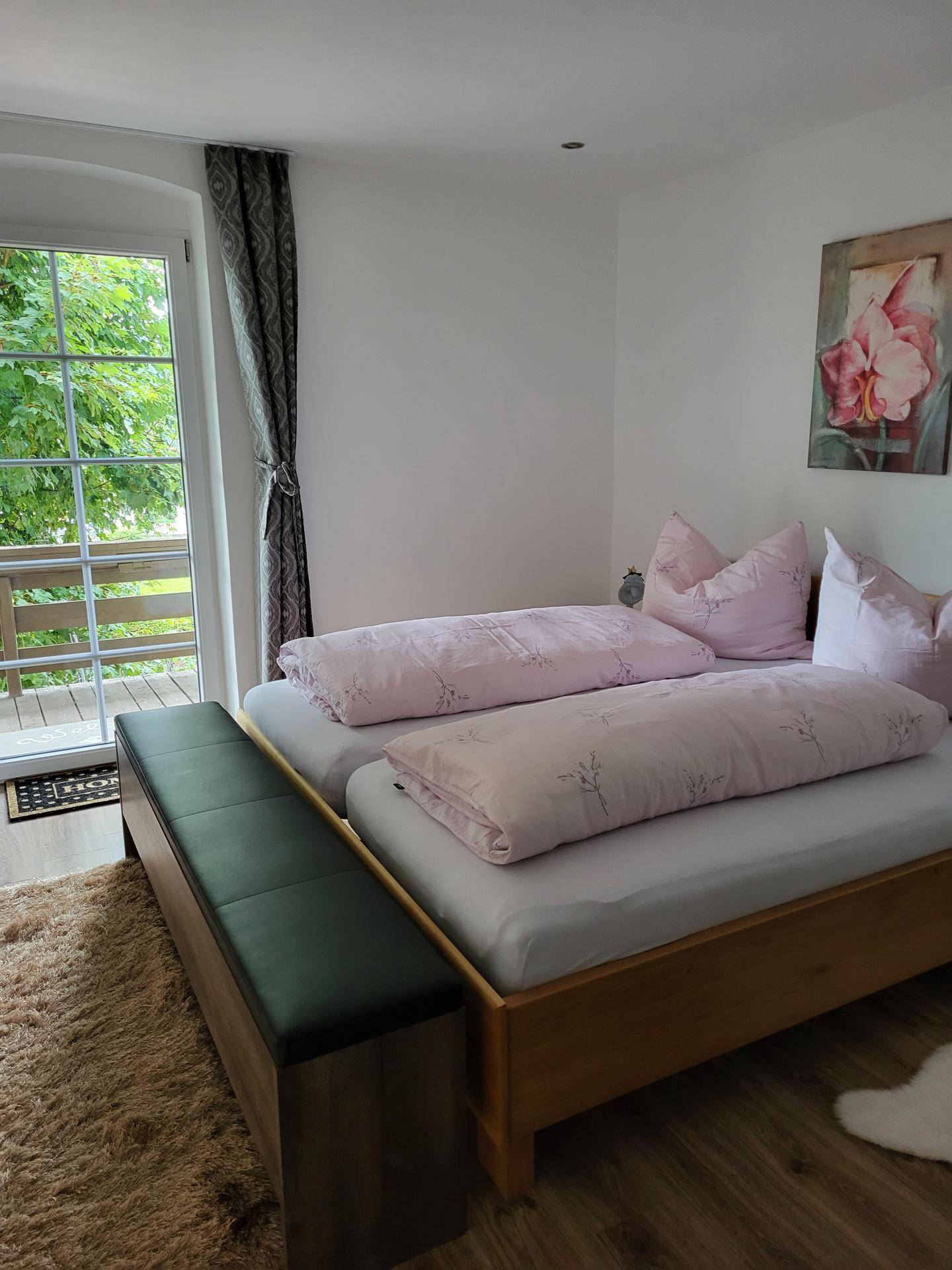 Helles Schlafzimmer mit zwei Einzelbetten, Holzboden und Zugang zu einem Balkon.