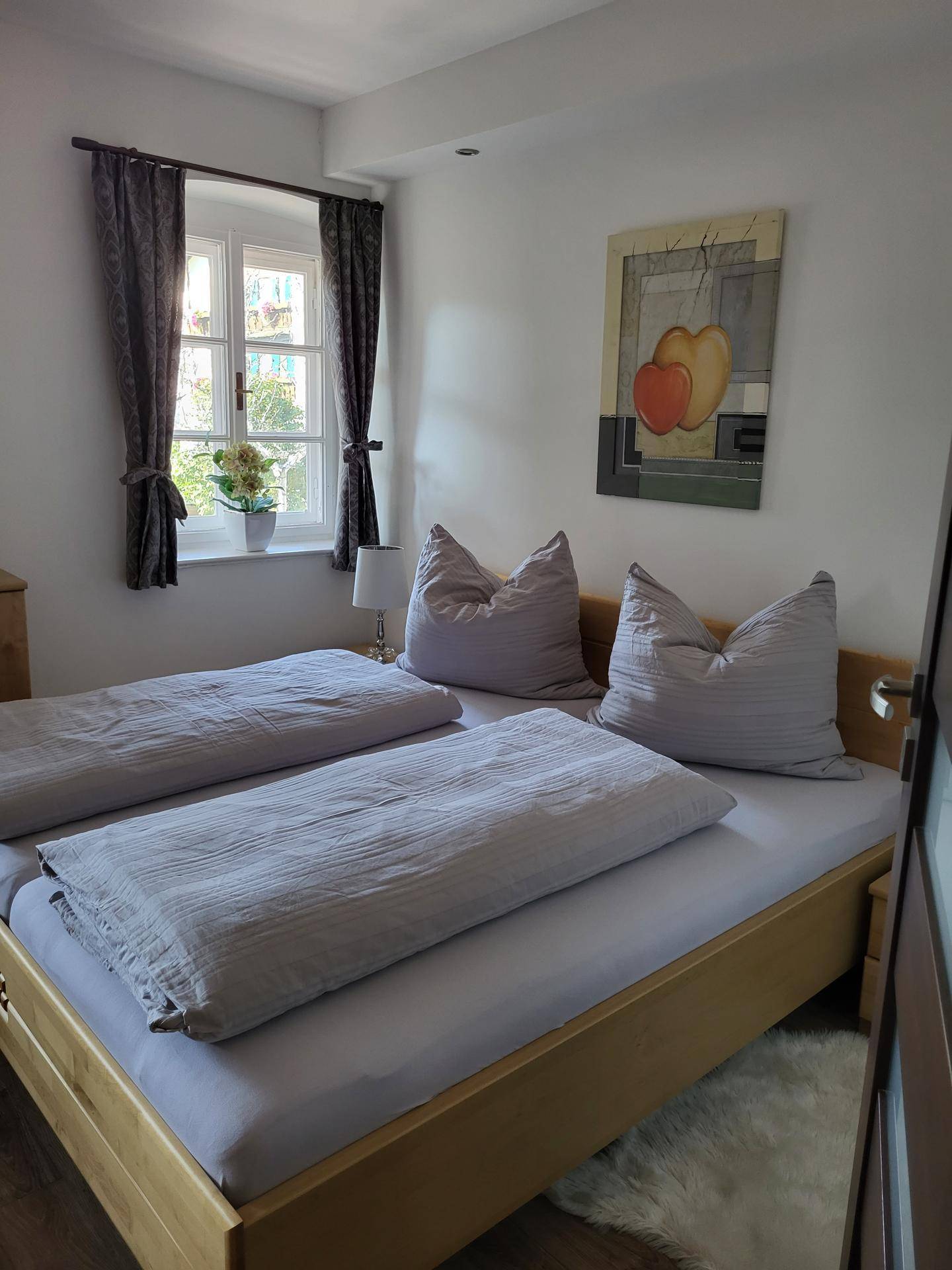Helles Schlafzimmer mit Doppelbett, Holzboden und Fenster mit Blick nach draußen.