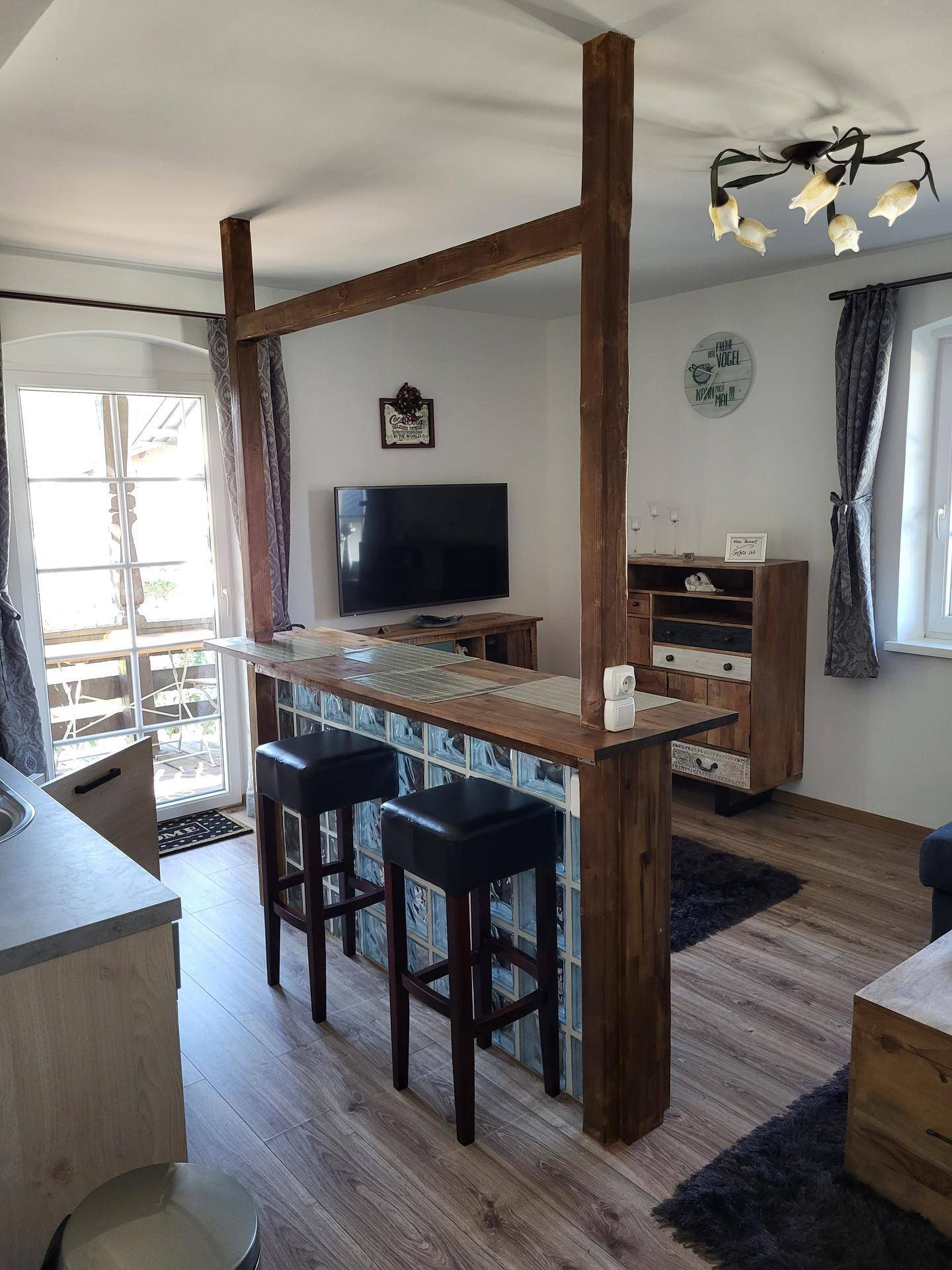 Offener Wohnbereich mit Frühstücksbar, Fernseher und Zugang zu einem Balkon.