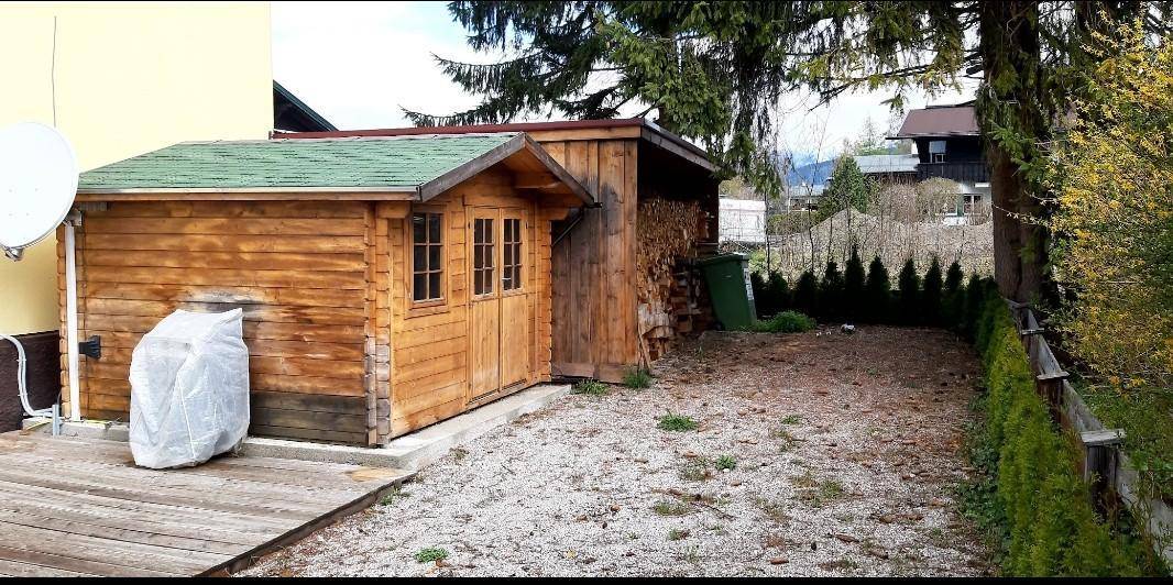 Hölzerner Gartenschuppen mit grünem Dach und angrenzendem Holzschuppen im Garten.